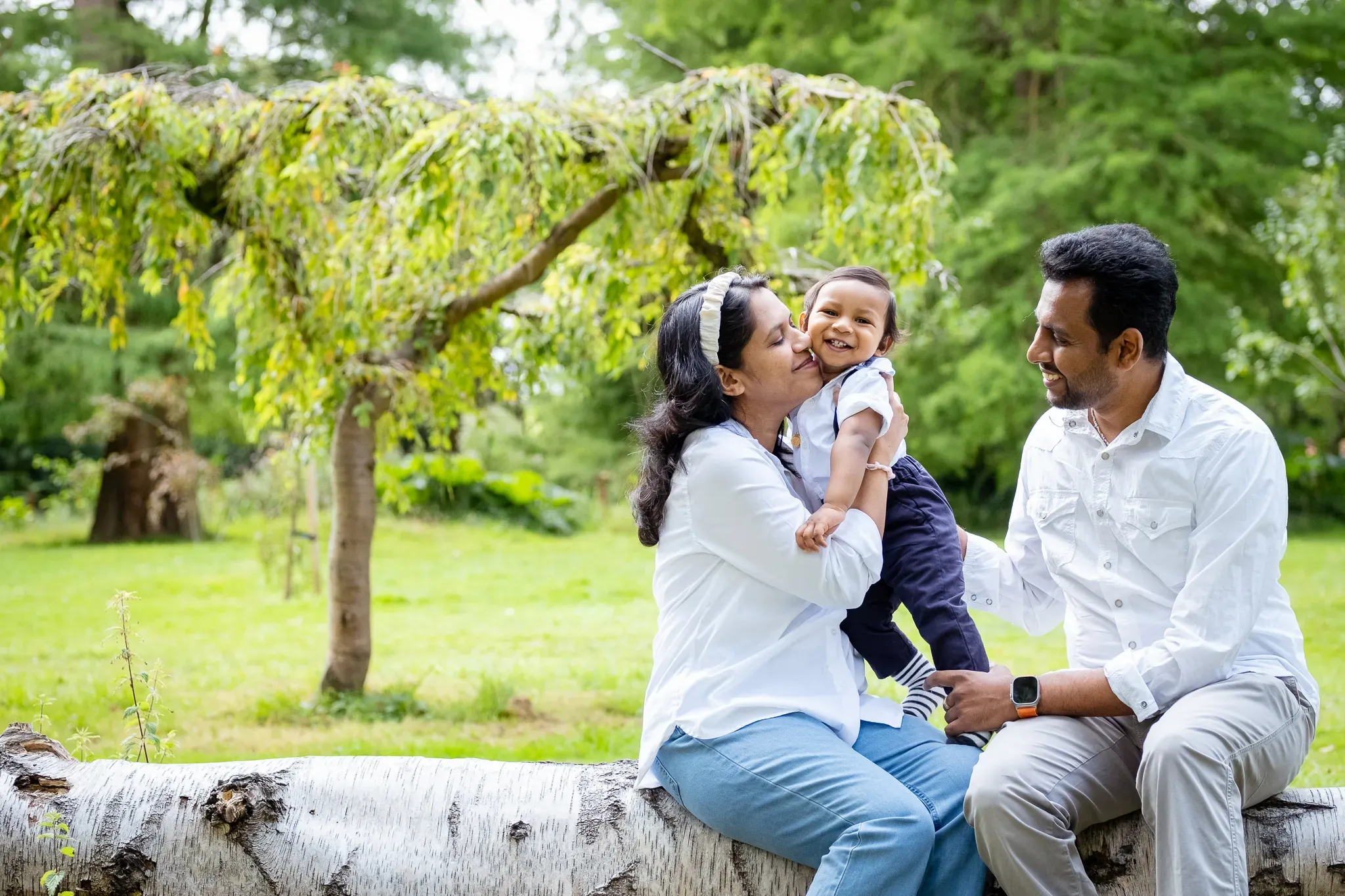 Family of three sitting on a tree, mum kissing her son, dad looking at them