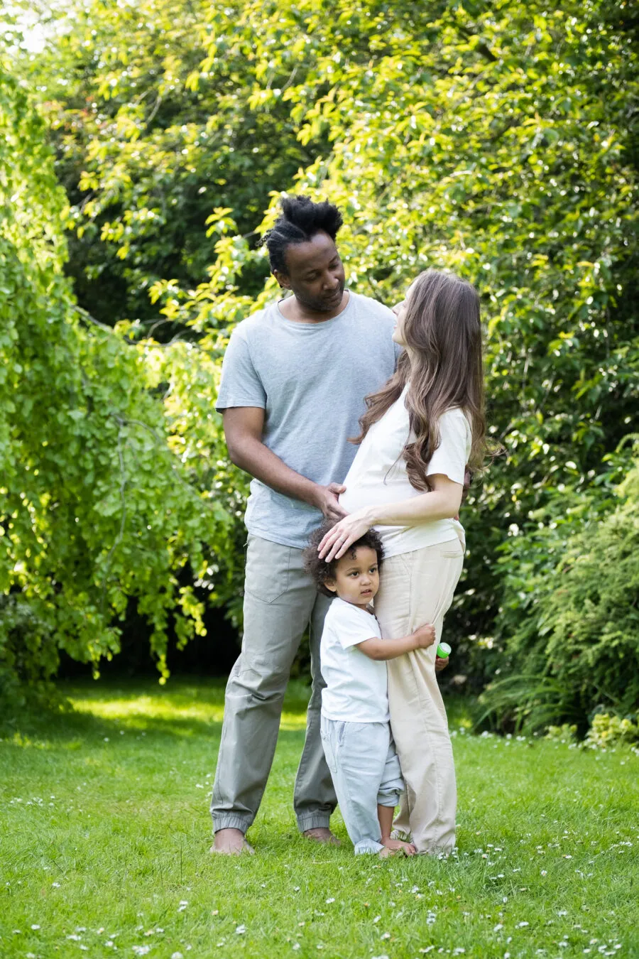 Family of three, soon to be four in a park, enjoying time together while taking a photoshoot