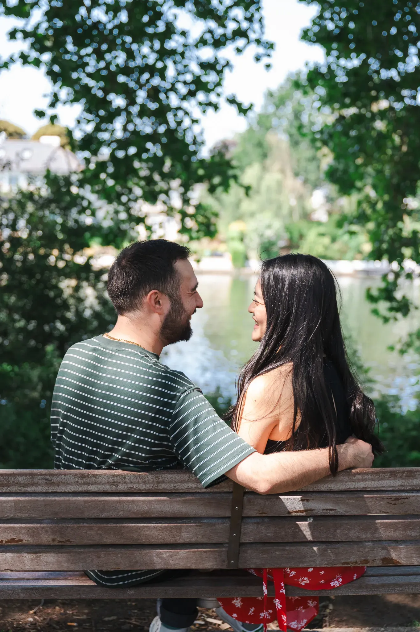 Couple sitting on a bench, looking at each other, love couple photoshoot, photo session by river Thames in Canbury gardens in Kingston, London