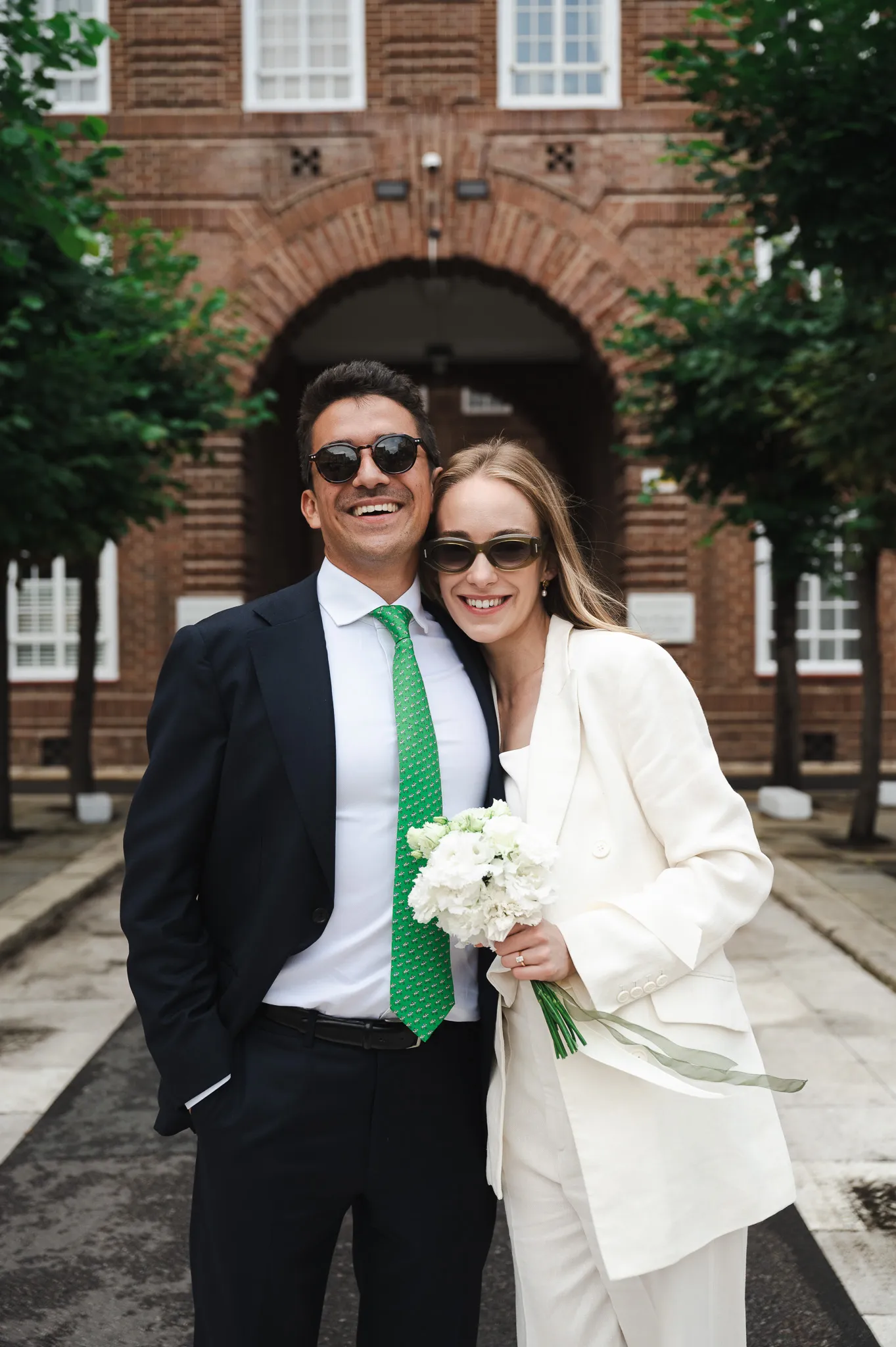 A smiling couple in sunglasses stands outdoors