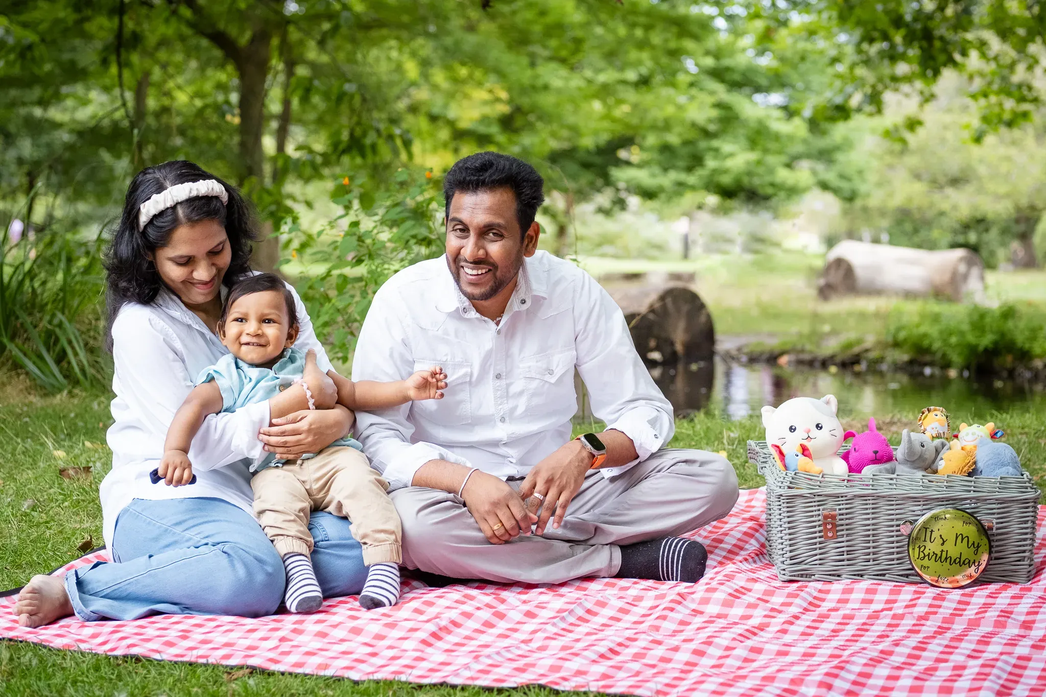 Family of three on a picnic in a park, celebrating baby boy's first birthday