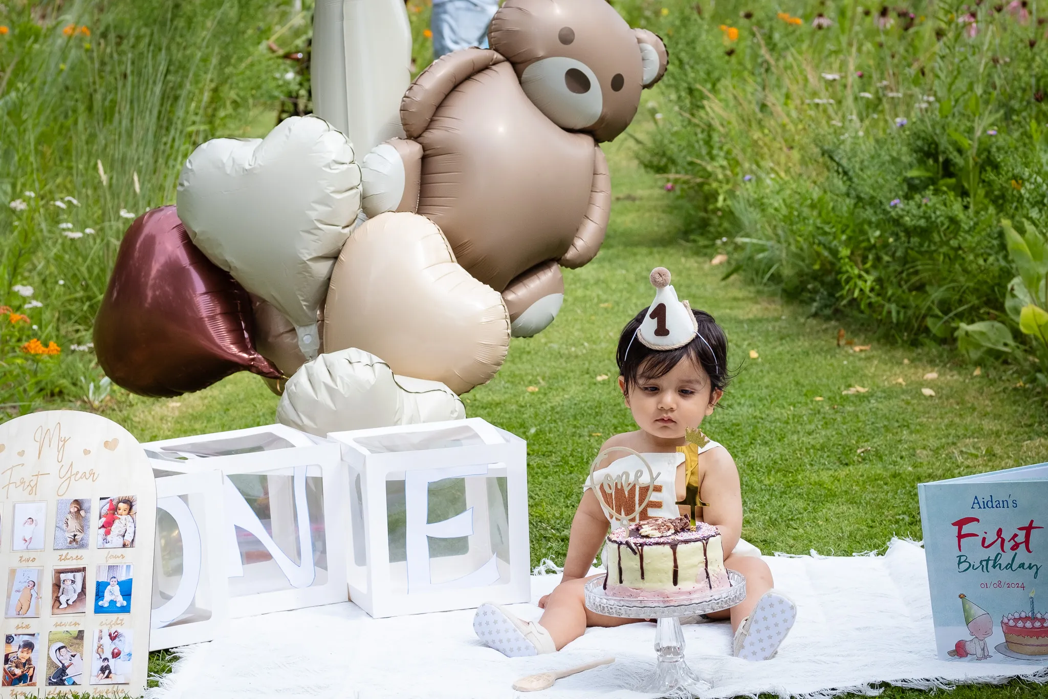 Little baby boy's first birthday photoshoot in a park, cake smash on a picnic, birthday decoration, balloons