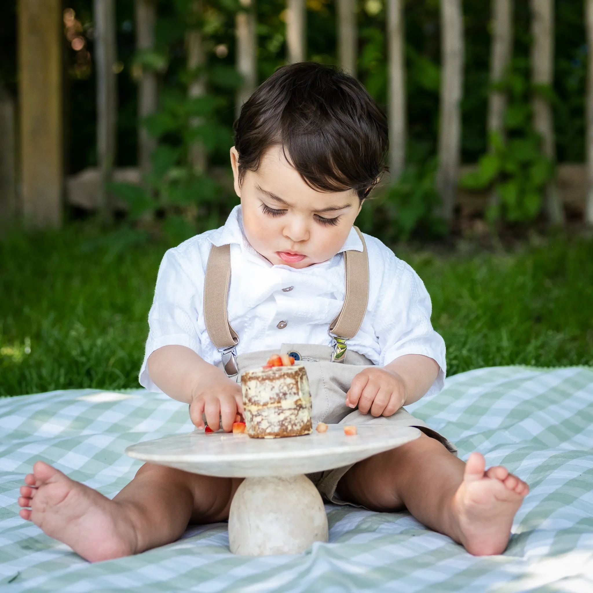 Little boy for his first birthday for a outdoor cake smash photoshoot in the park on a picnic blanket