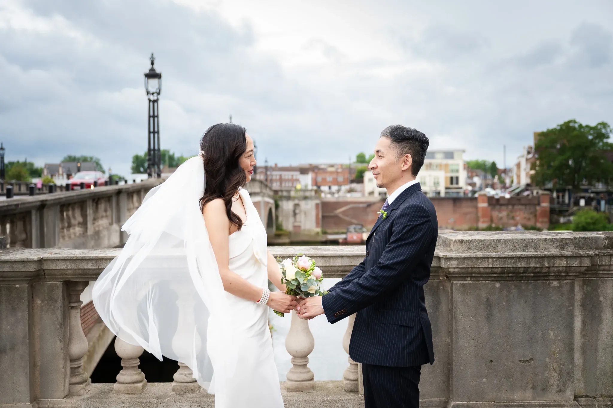 Bride and groom smiling at each other on a stone bridge