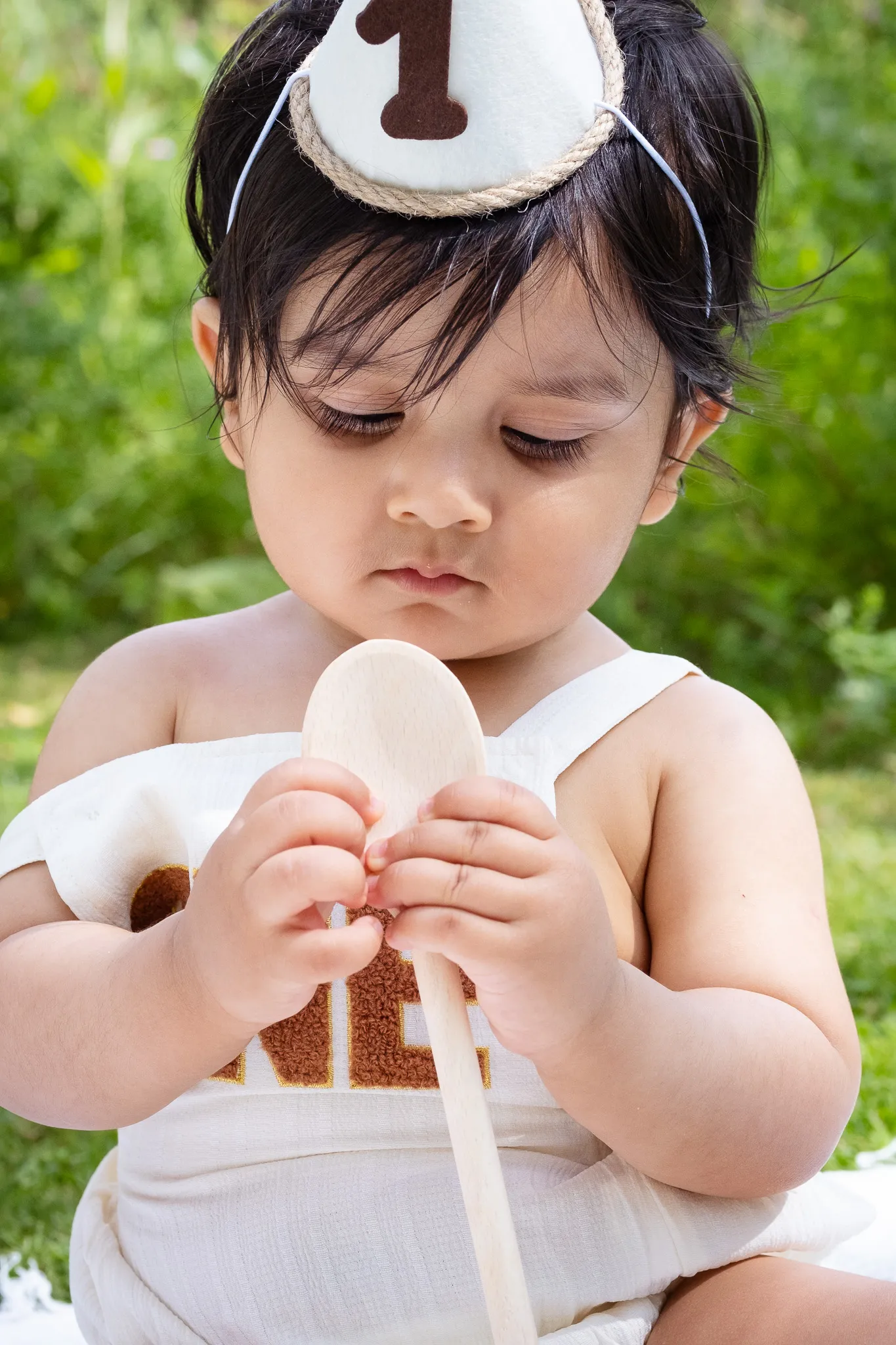 Little baby boy's first birthday photoshoot in a park, holding wooden spoon, having a cake smash on a picnic, birthday decoration, balloons