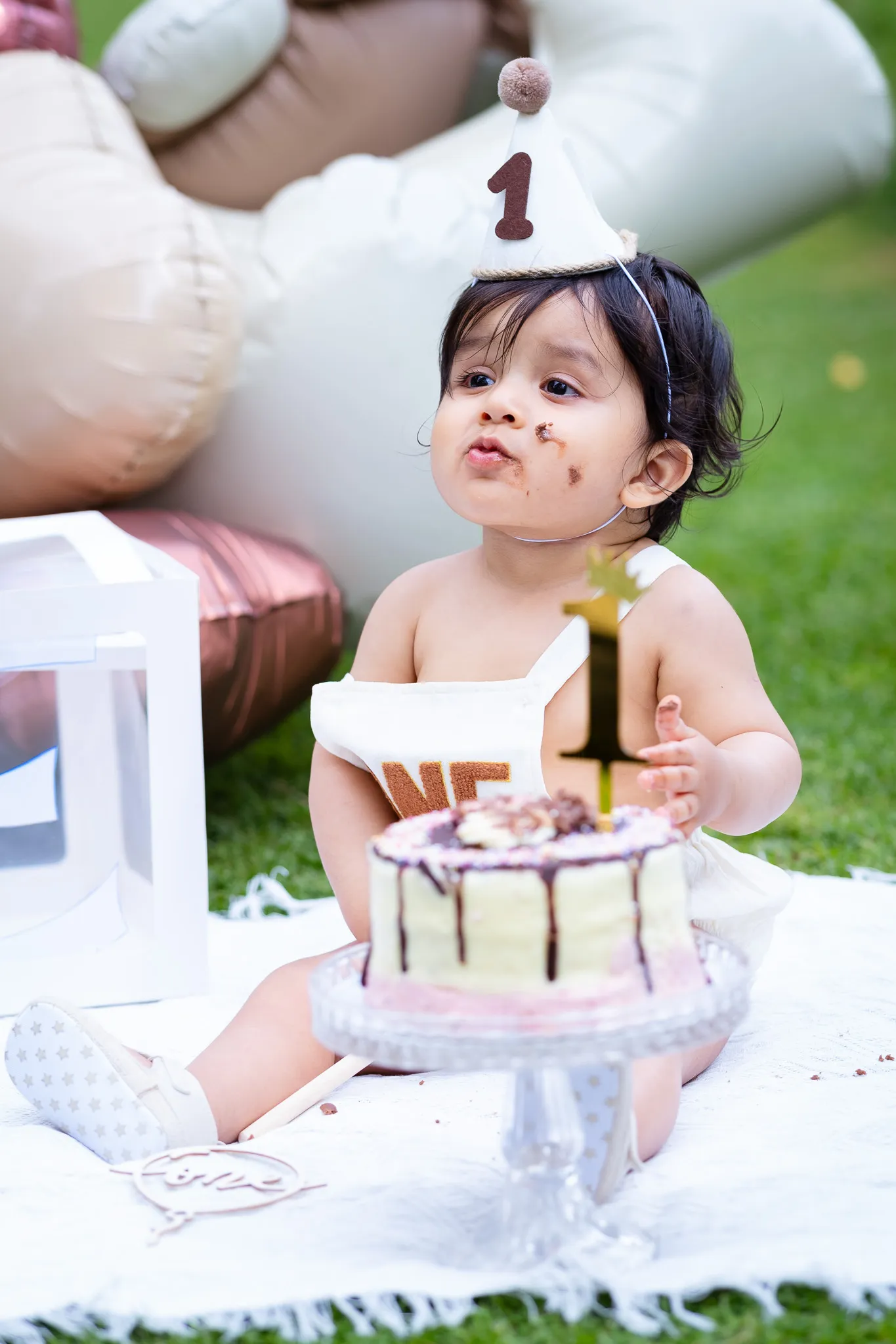 Little baby boy's first birthday photoshoot in a park, cake smash on a picnic, birthday decoration, balloons