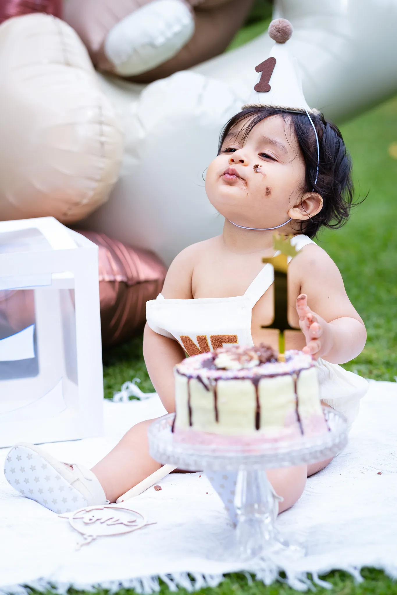 Little baby boy's first birthday photoshoot in a park, cake smash on a picnic, birthday decoration, balloons