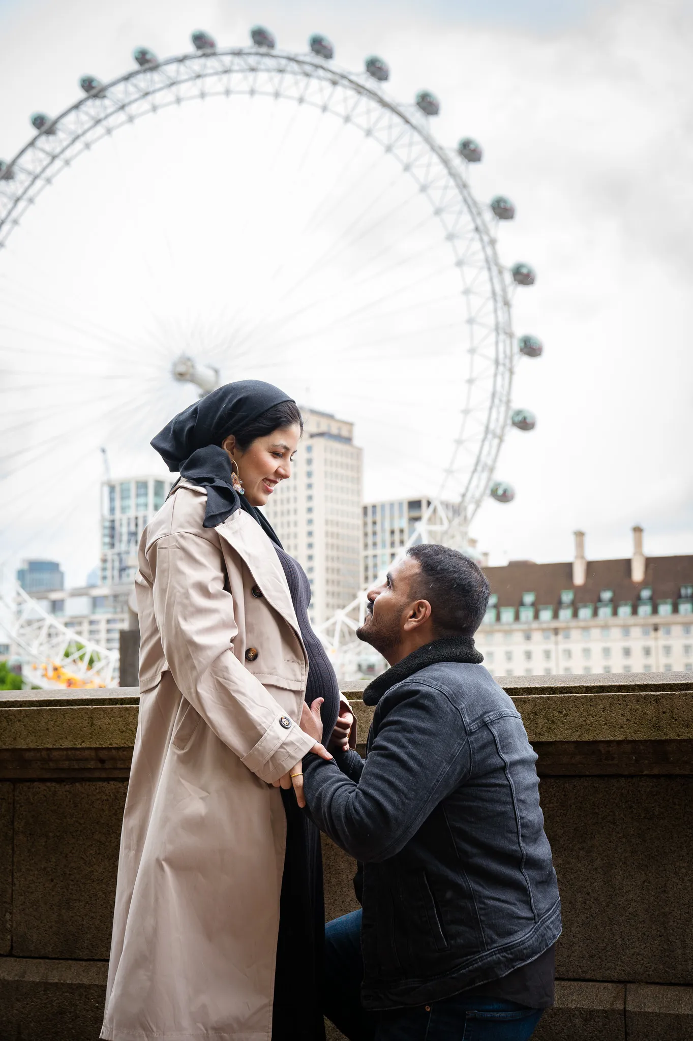 Love couple the man is kneeing in front of his wife, holding here hands, doing a maternity photoshoot in London