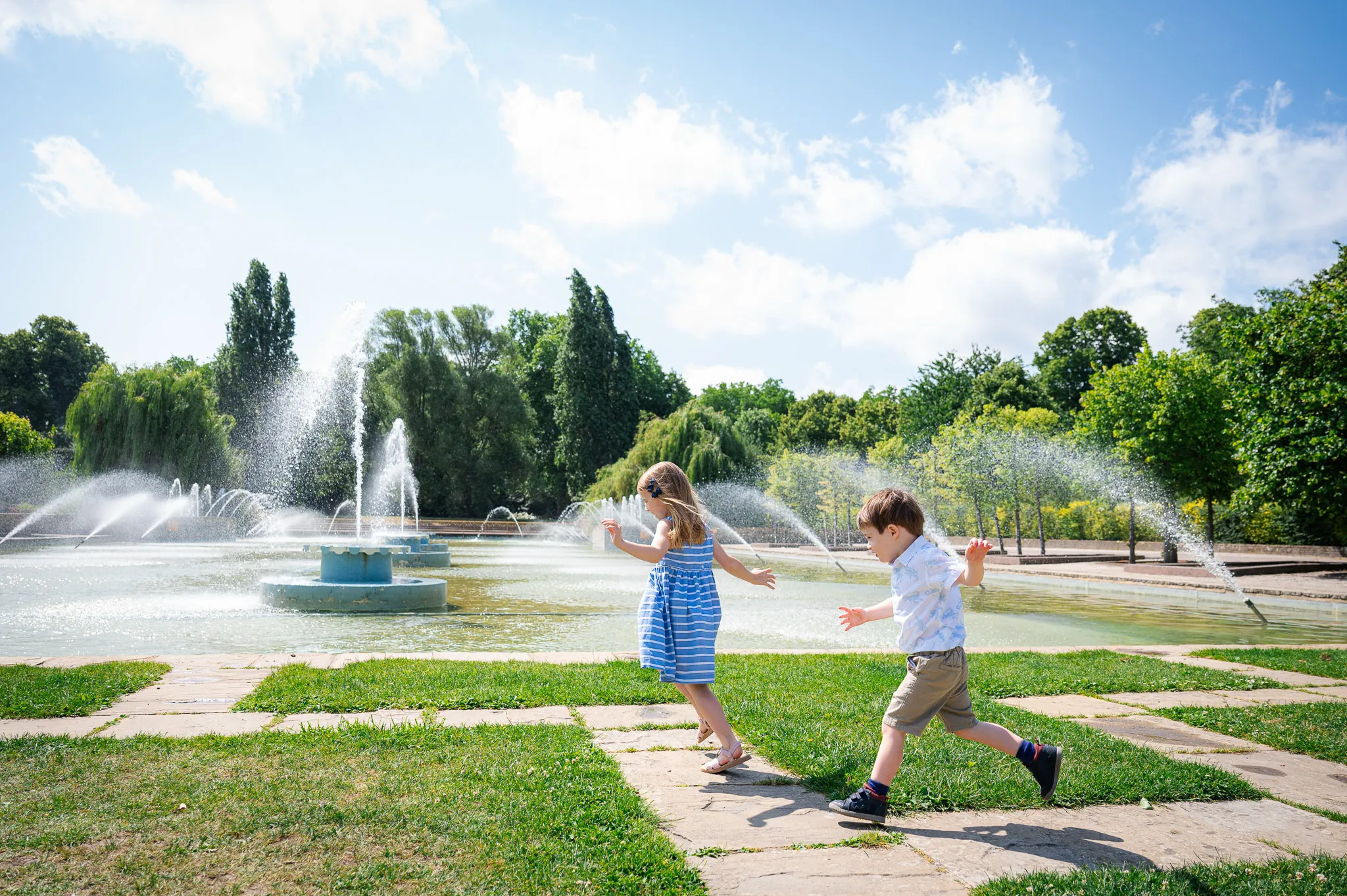 Brother and sister running and playing by the fountains in Battersea Park