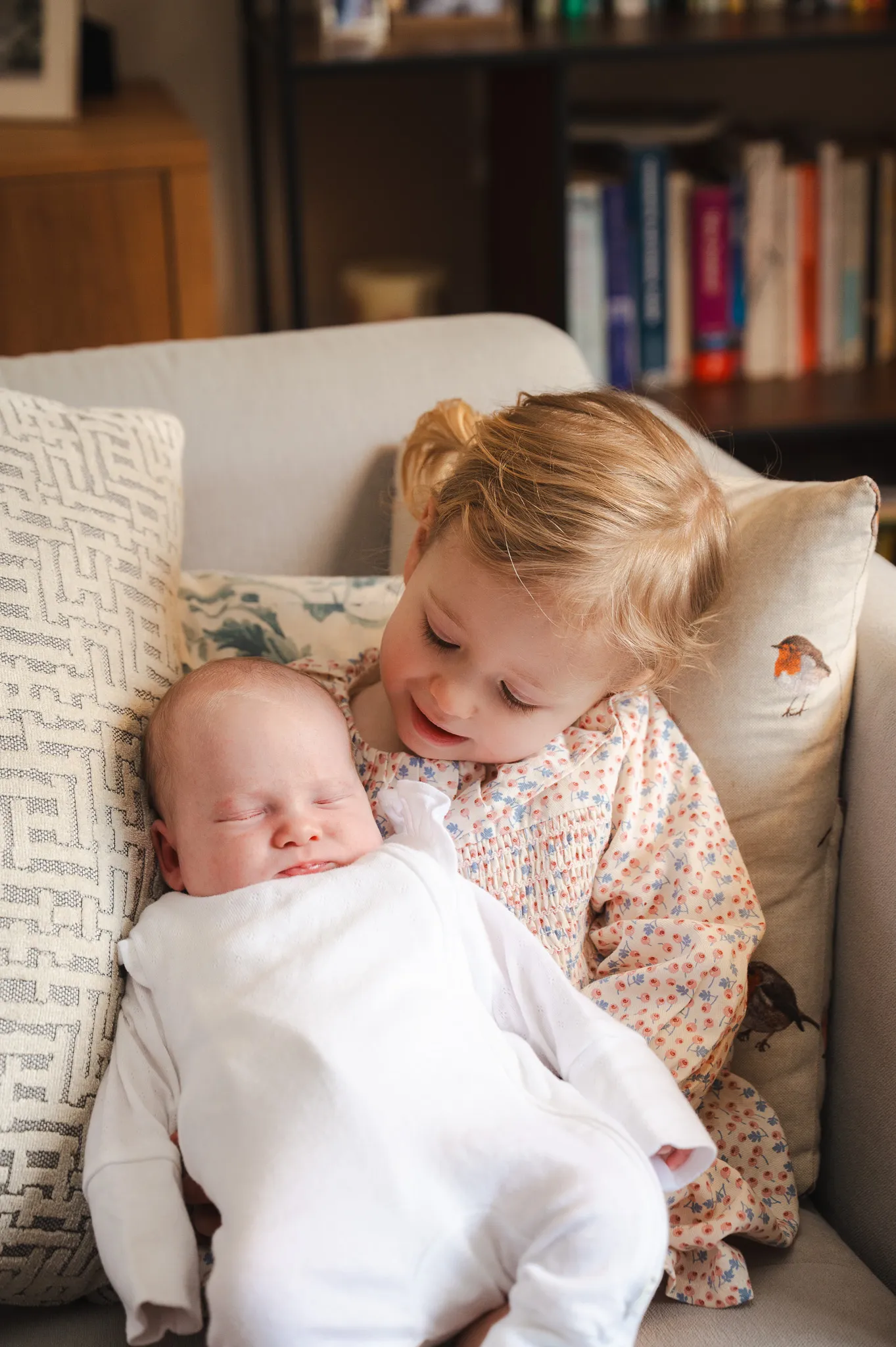 Big sister cuddling her newborn baby sibling on the sofa