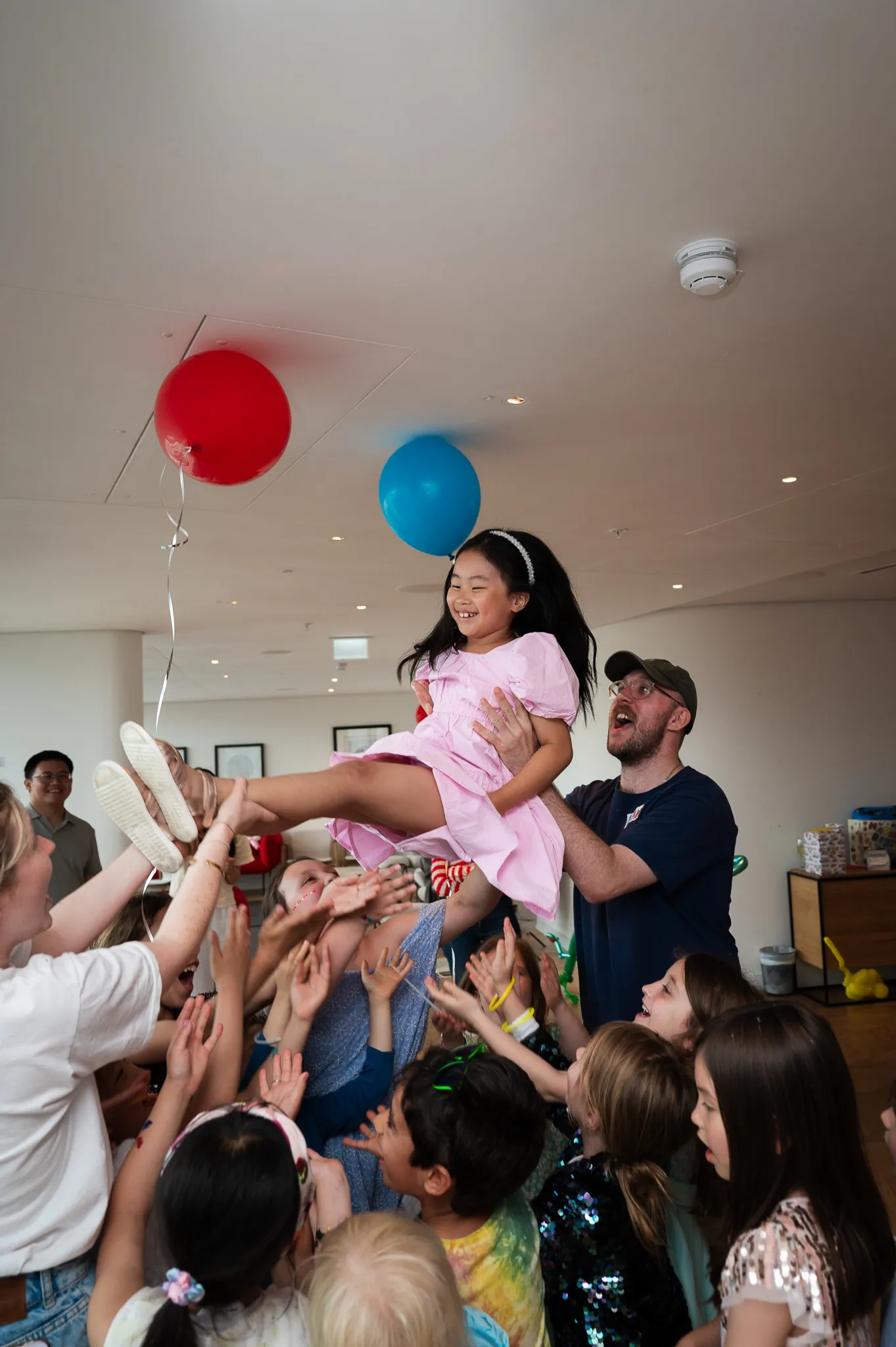 Birthday girl being lifted into the air by laughing party guests