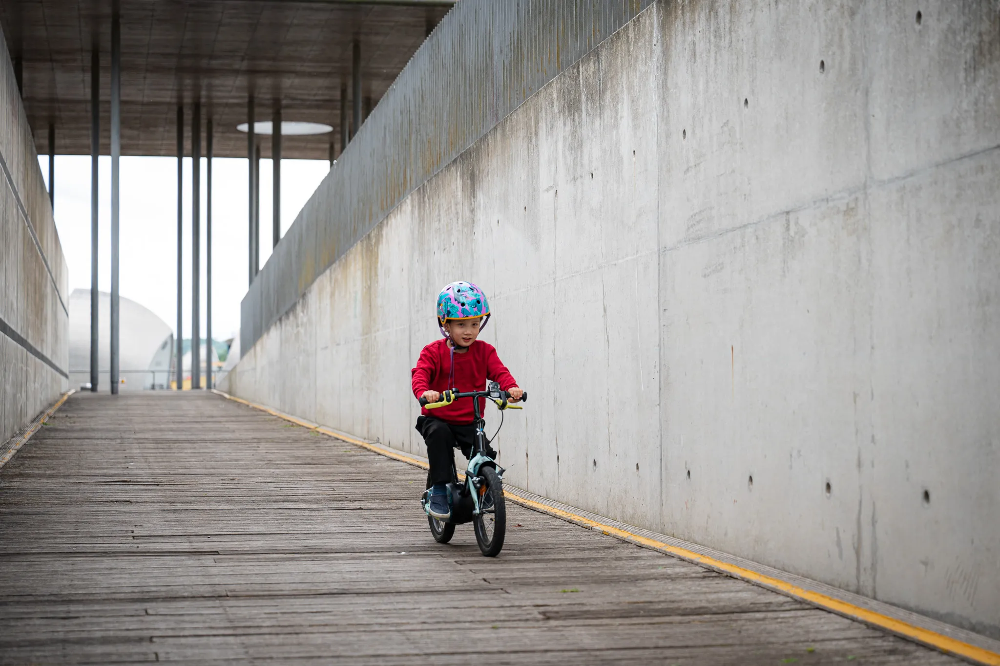 Little boy in a helmet riding his balance bike along a concrete walkway
