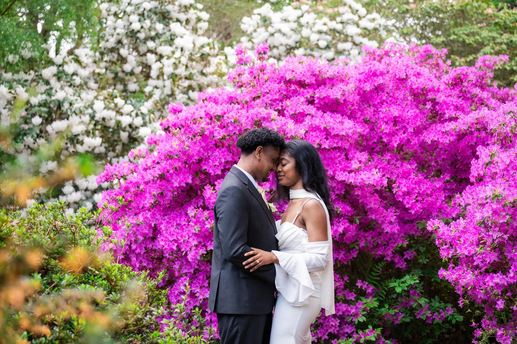 Couple touching foreheads in front of bright pink azaleas and white rhododendrons