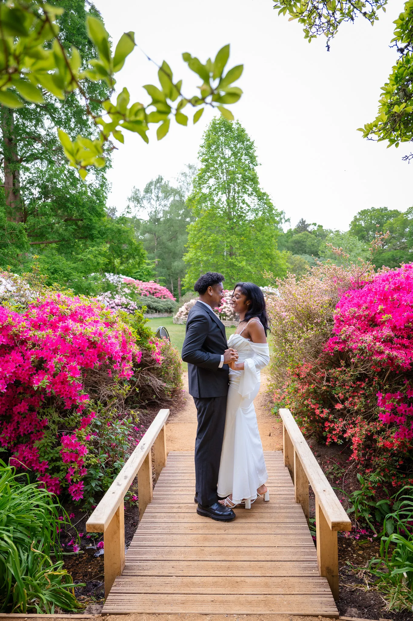 Couple embracing on a wooden bridge between bright pink azaleas