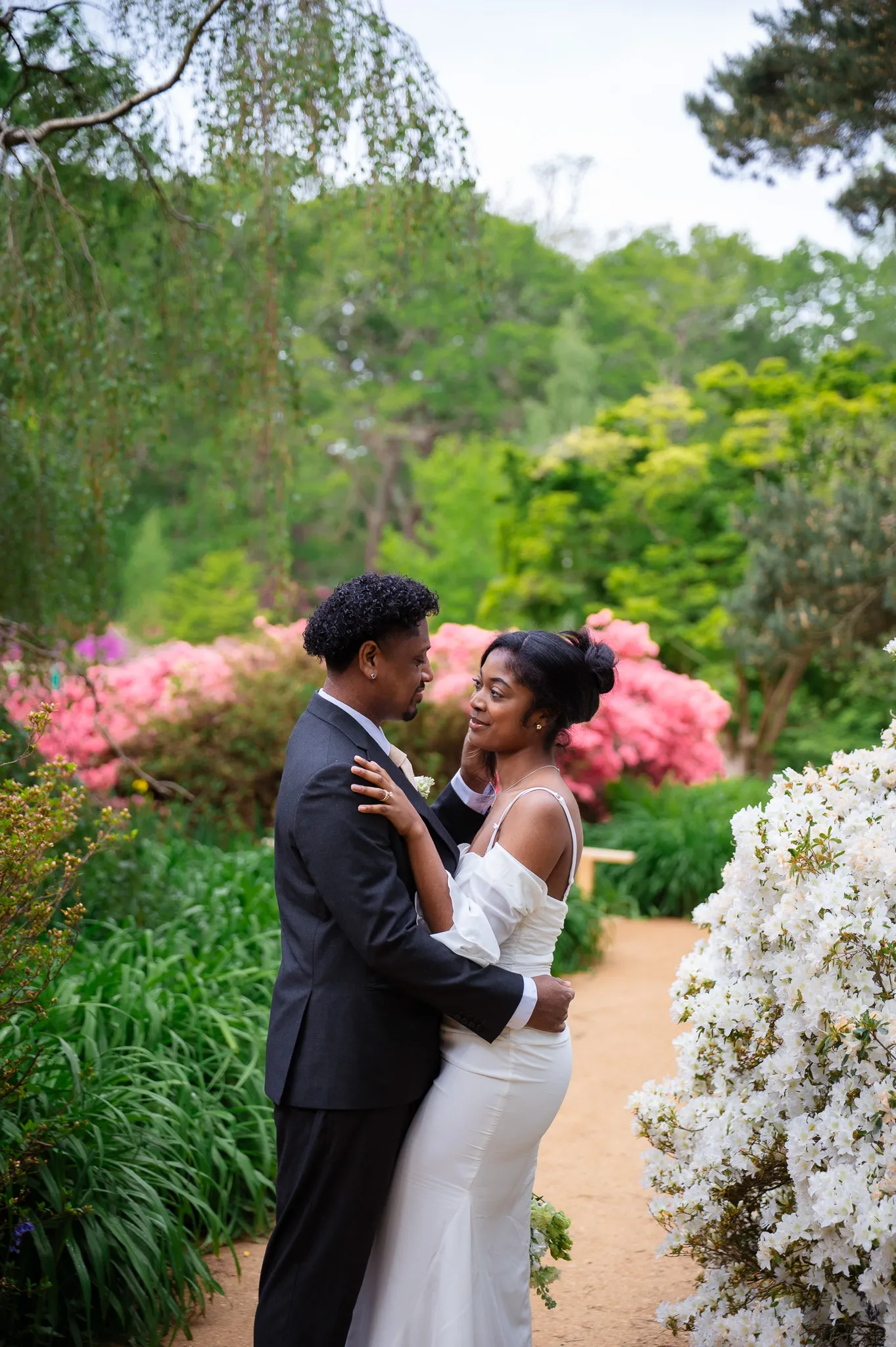 Couple in a gentle embrace on a garden path surrounded by pink and white azaleas