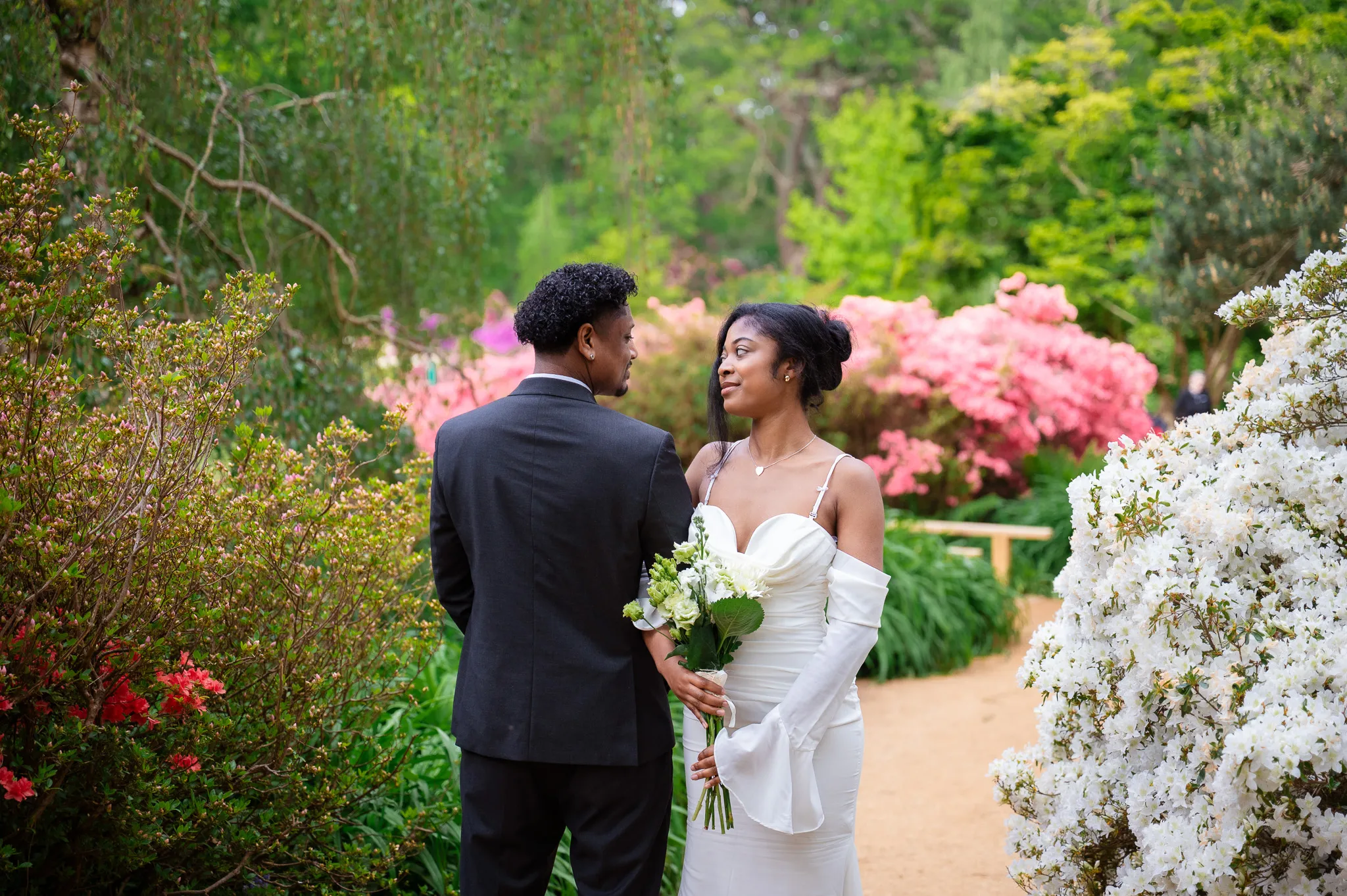 Bride holding her bouquet and smiling at the groom on a garden path lined with flowers