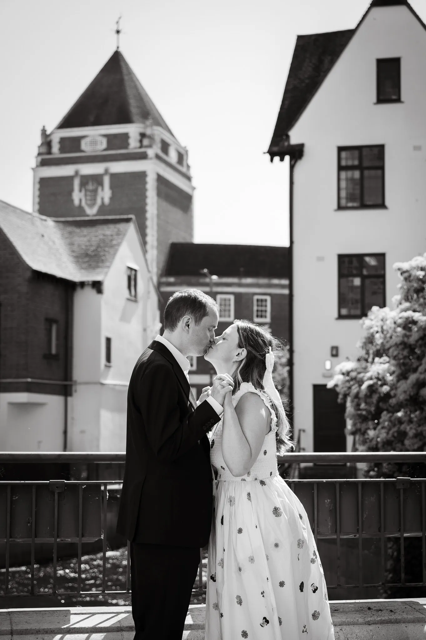 Black and white photo of a couple kissing on a bridge in front of historic buildings