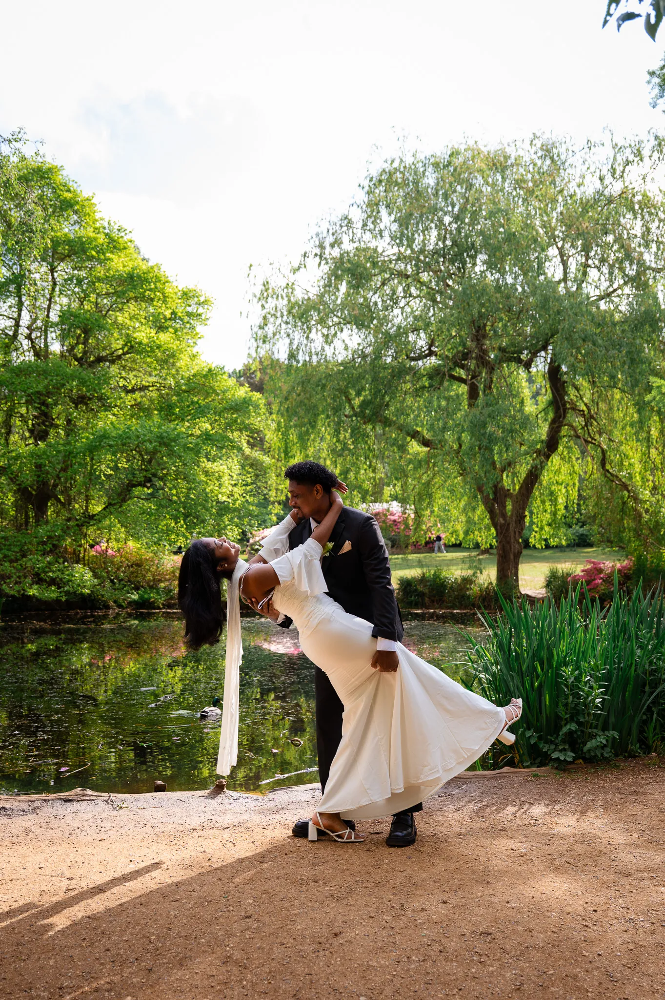 Groom dipping his bride by a lake in a sunlit garden