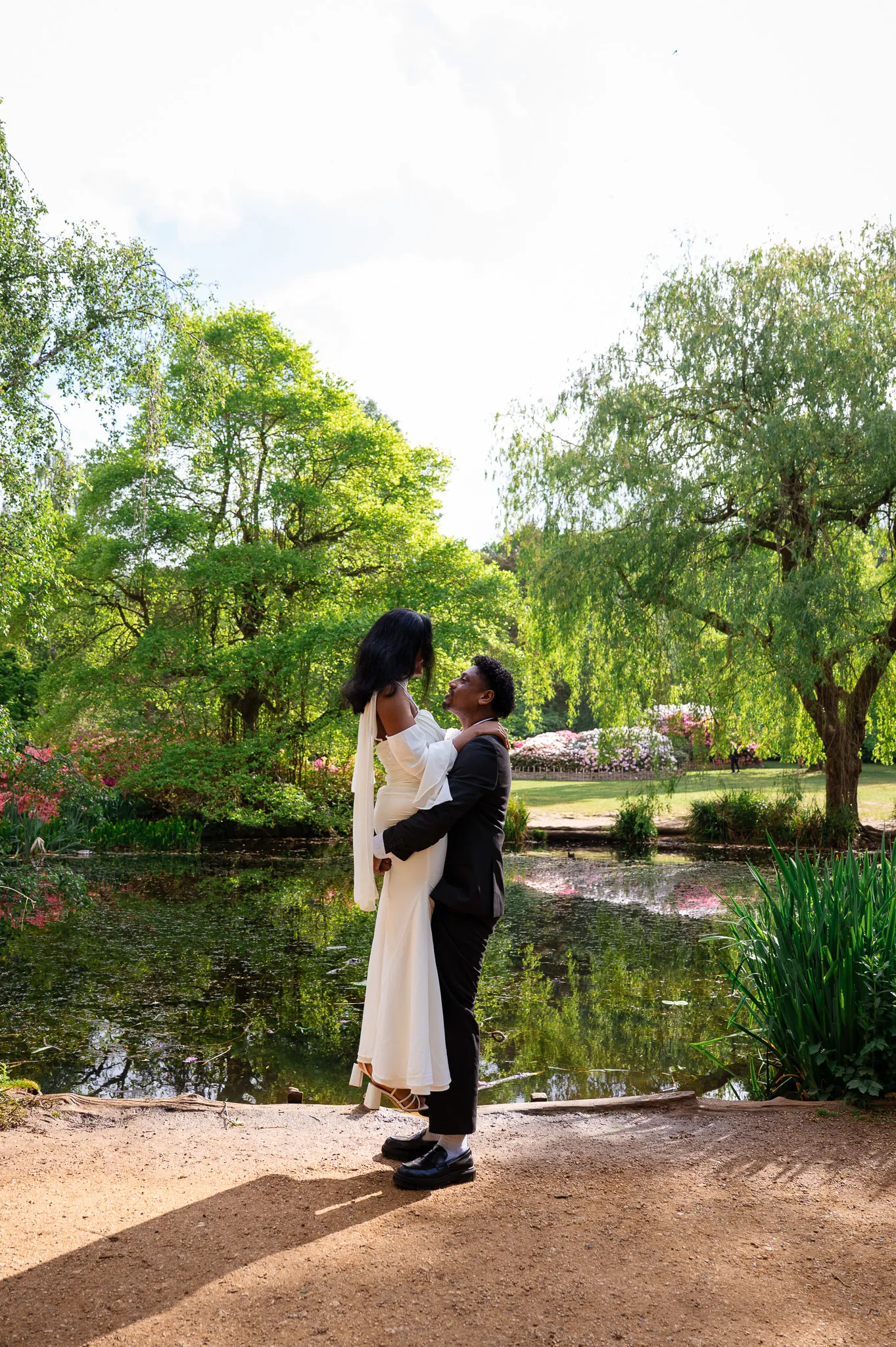 Groom lifting his bride in a hug beside a lake under willow trees