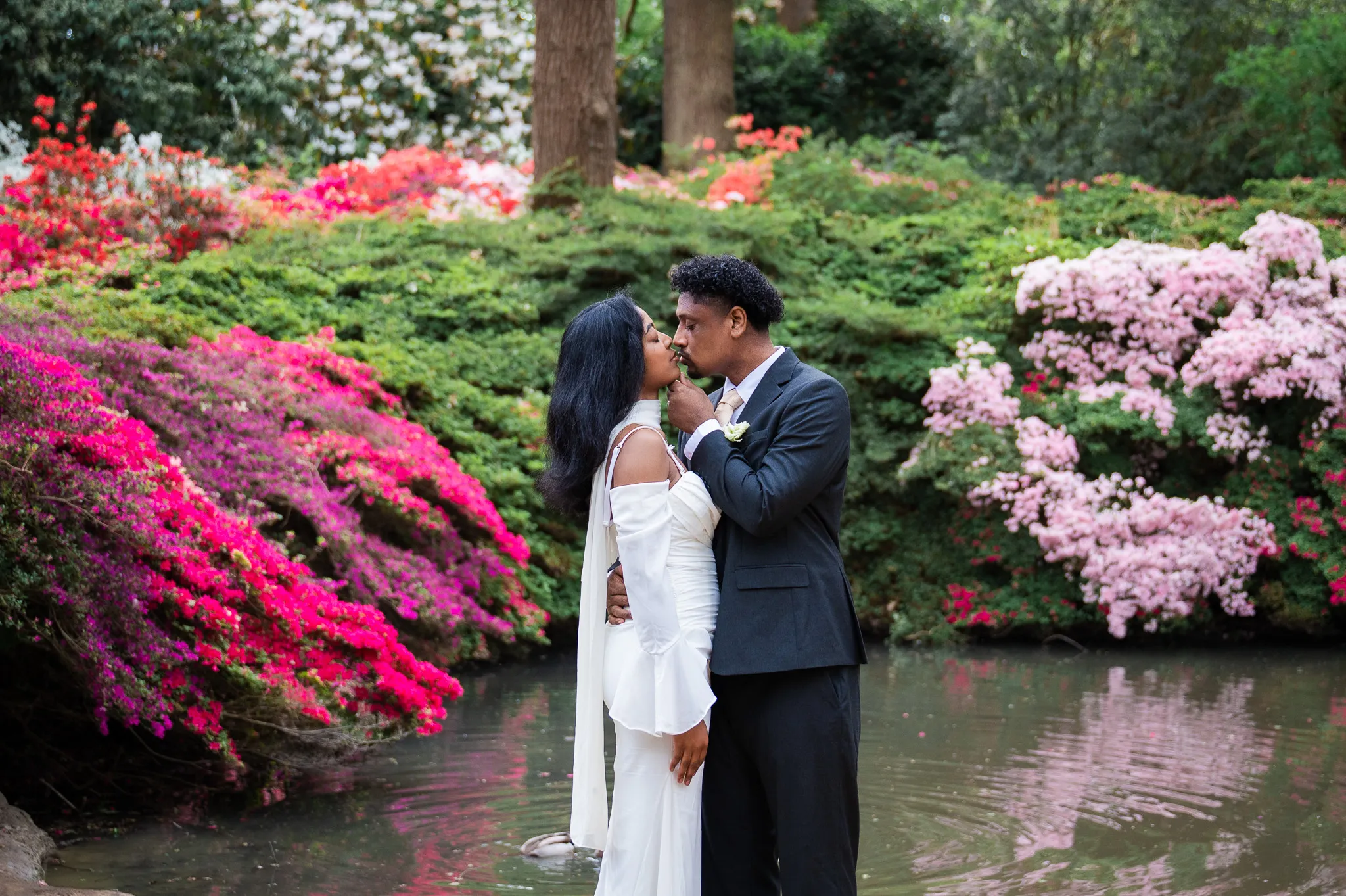 Couple sharing a tender moment beside a pond surrounded by pink azaleas