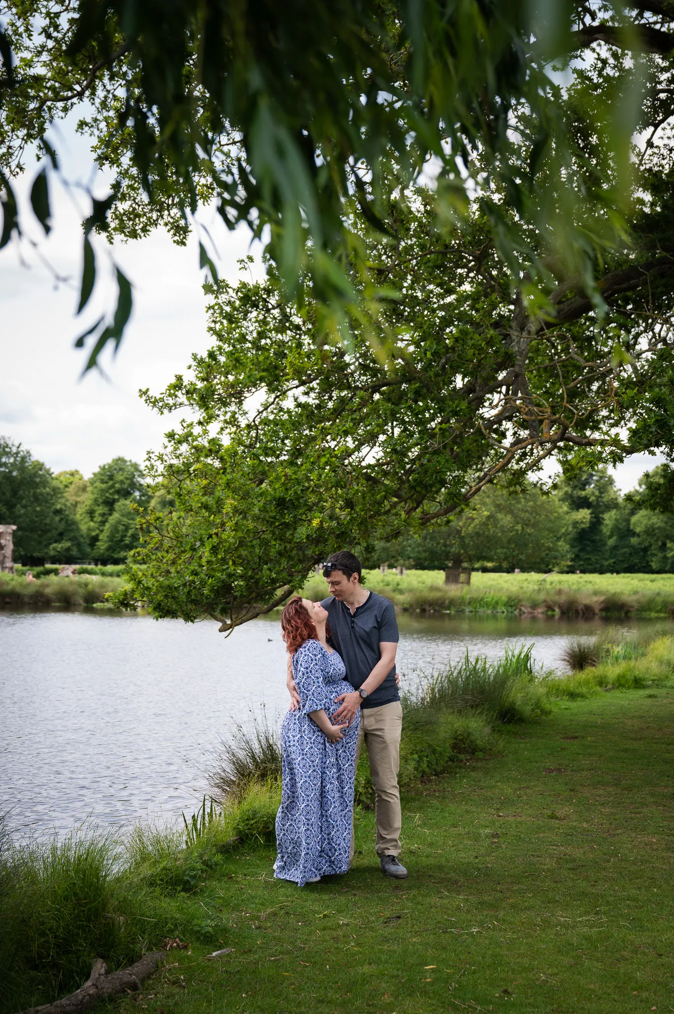 Expecting couple embracing by the river under the trees