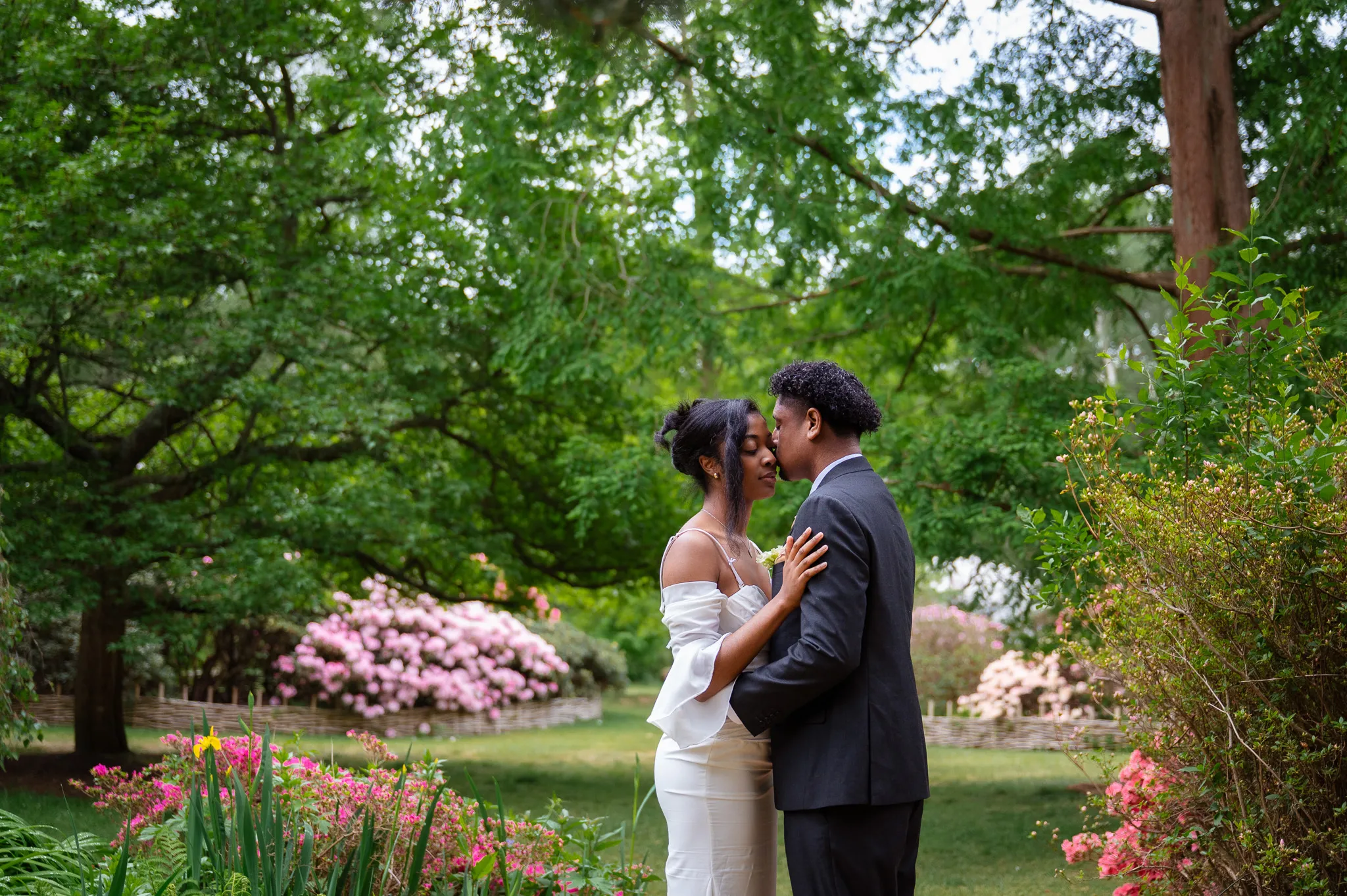 Couple embracing under tall green trees in a flower garden