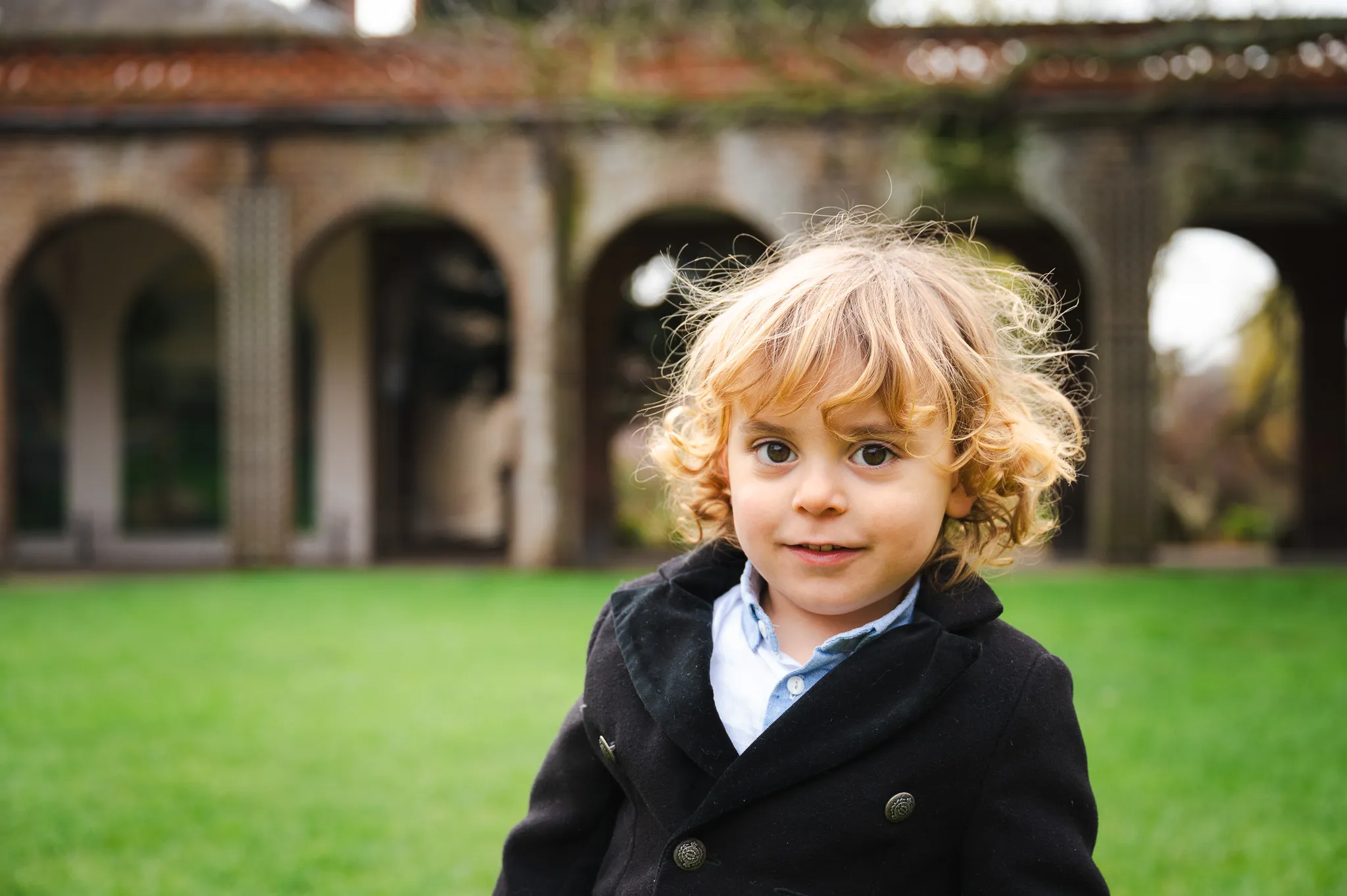 Curly-haired little boy in a smart coat in front of garden arches