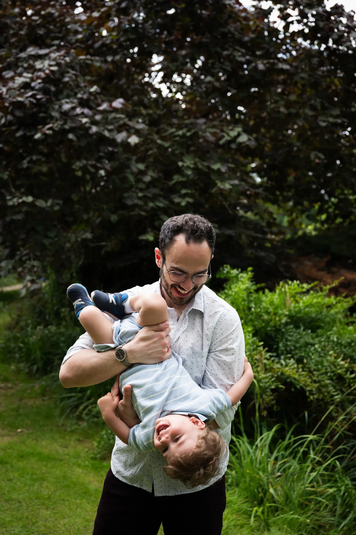 Dad holding his giggling toddler upside down in a garden