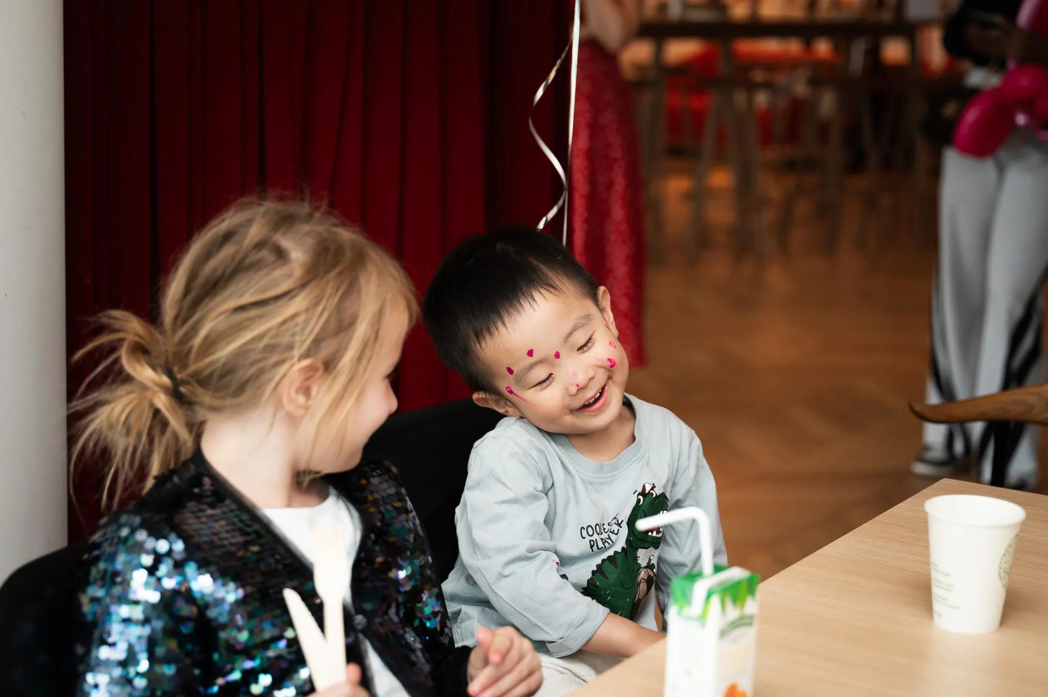 Little boy with face paint laughing with a friend at the party table