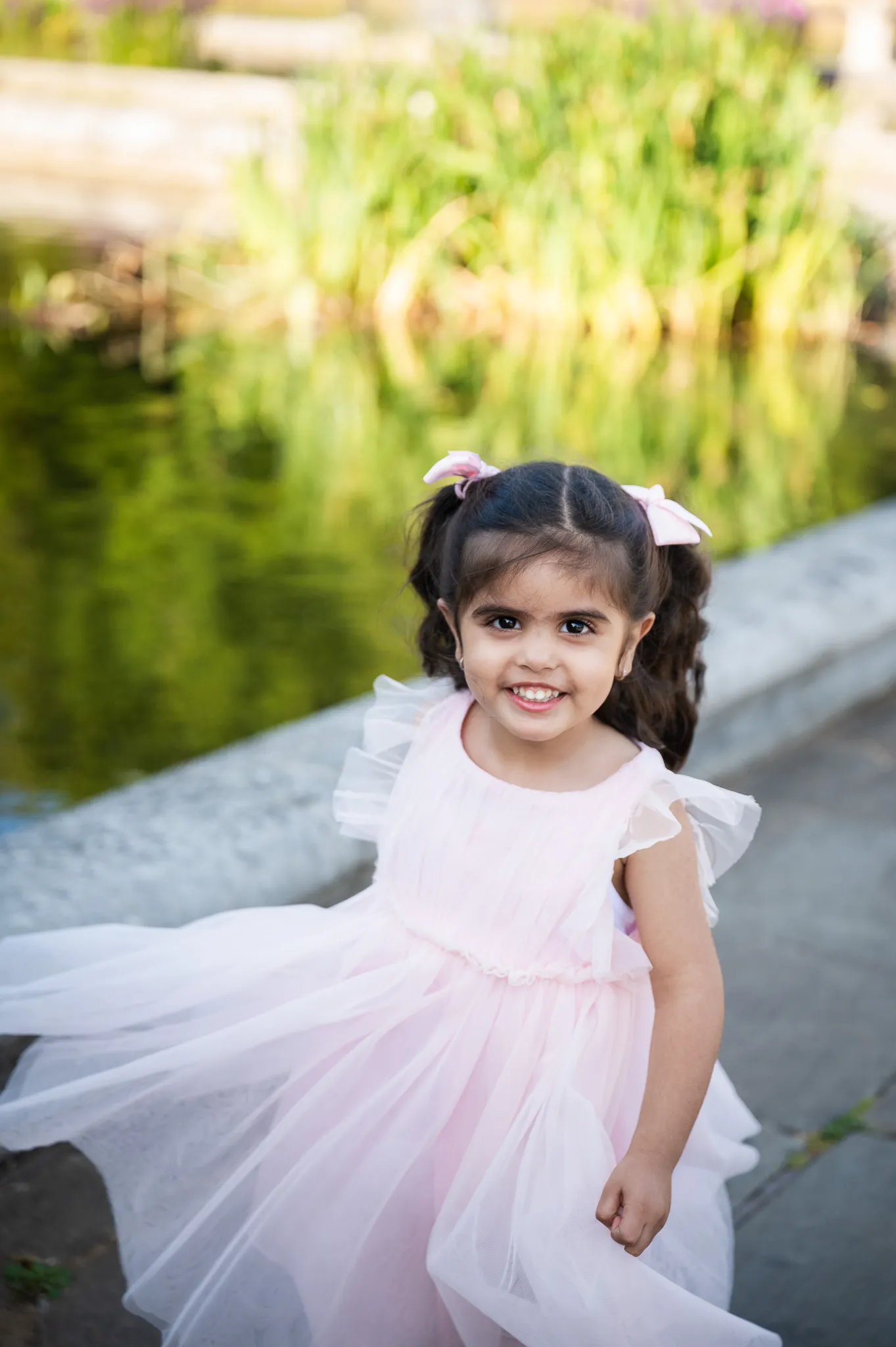 Smiling little girl in a pink tulle dress by the water