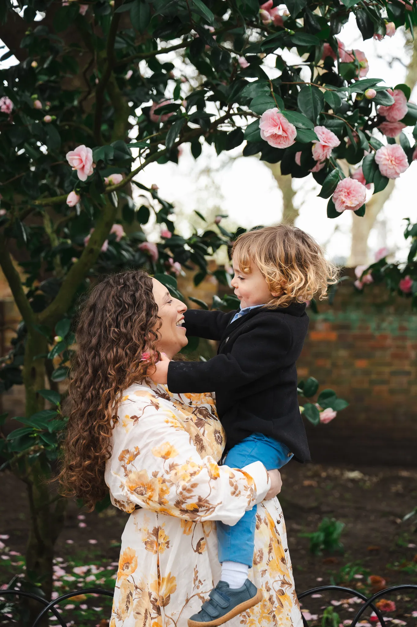 Pregnant mum smiling at her toddler among pink camellias