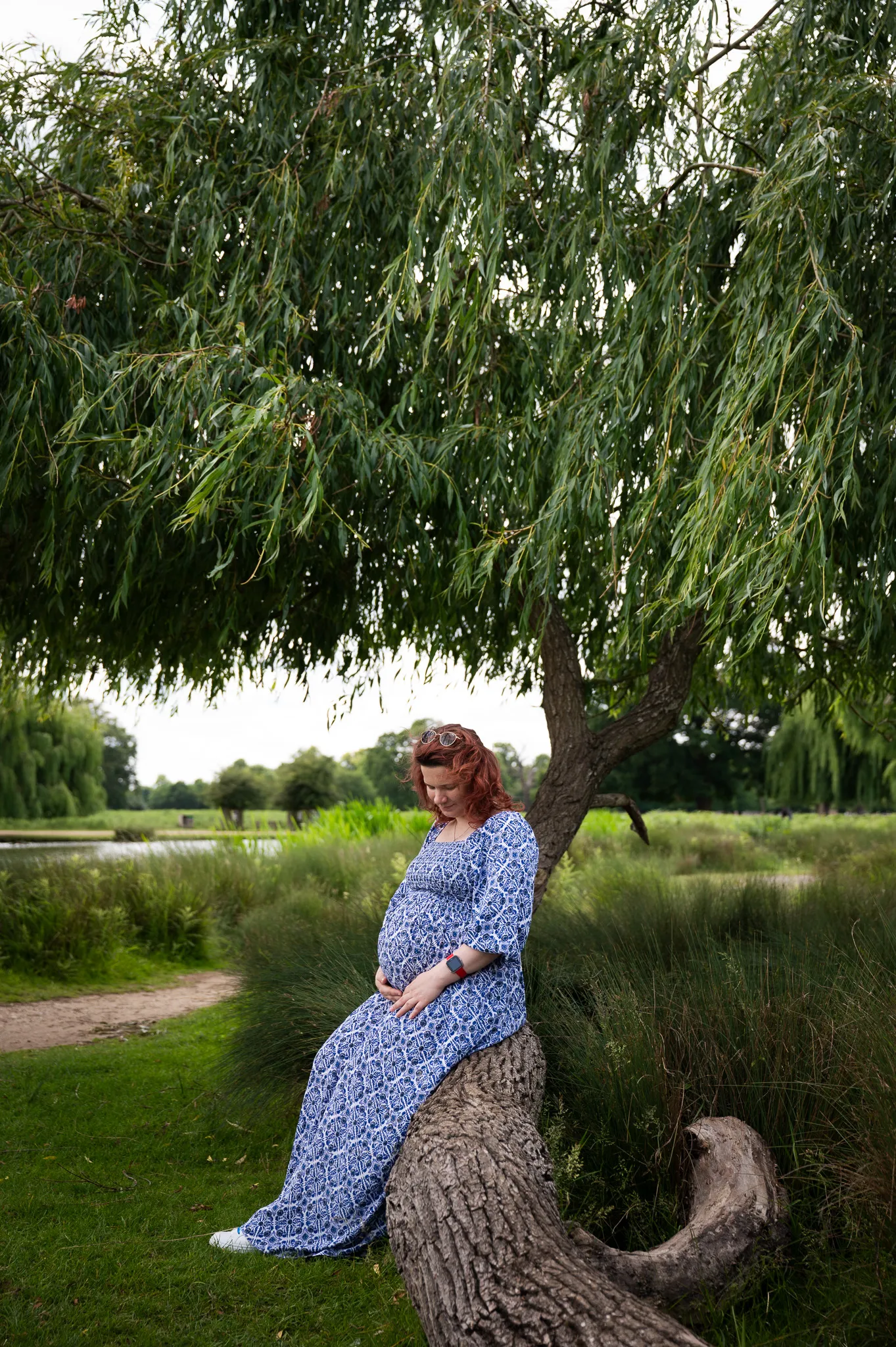 Pregnant mum sitting under a weeping willow cradling her bump