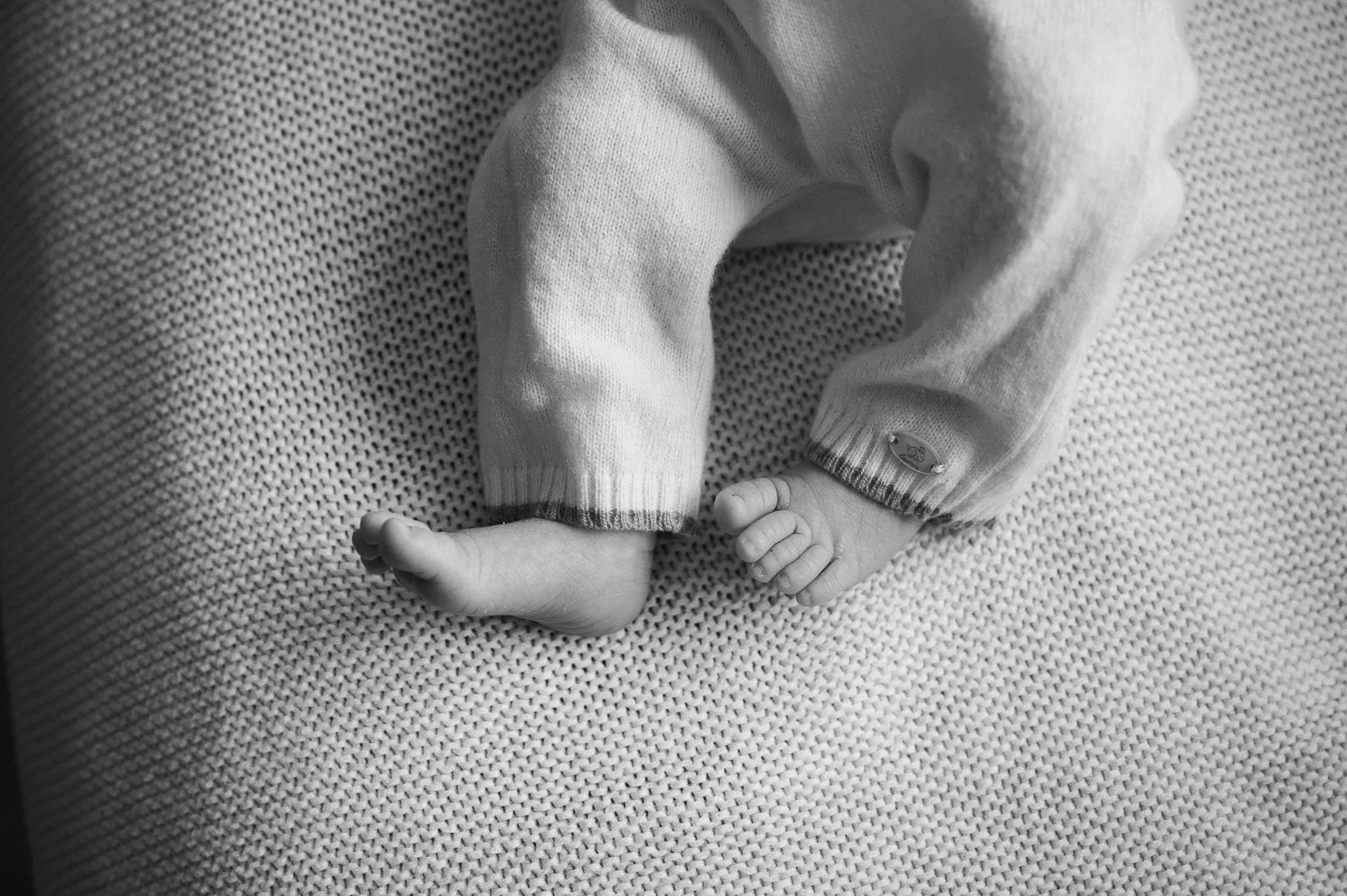 Black and white close-up of a newborn baby's tiny feet on a knitted blanket