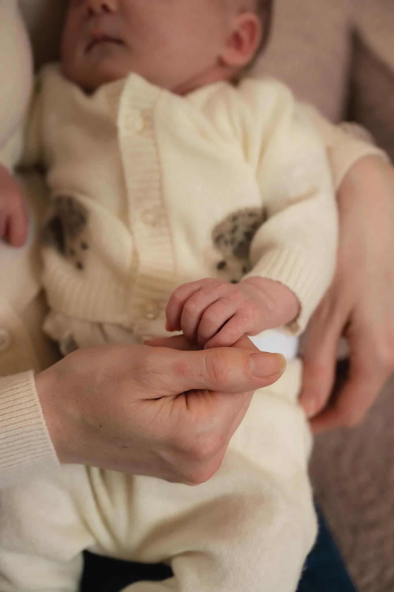 Newborn baby in a cream knit outfit holding a parent's finger