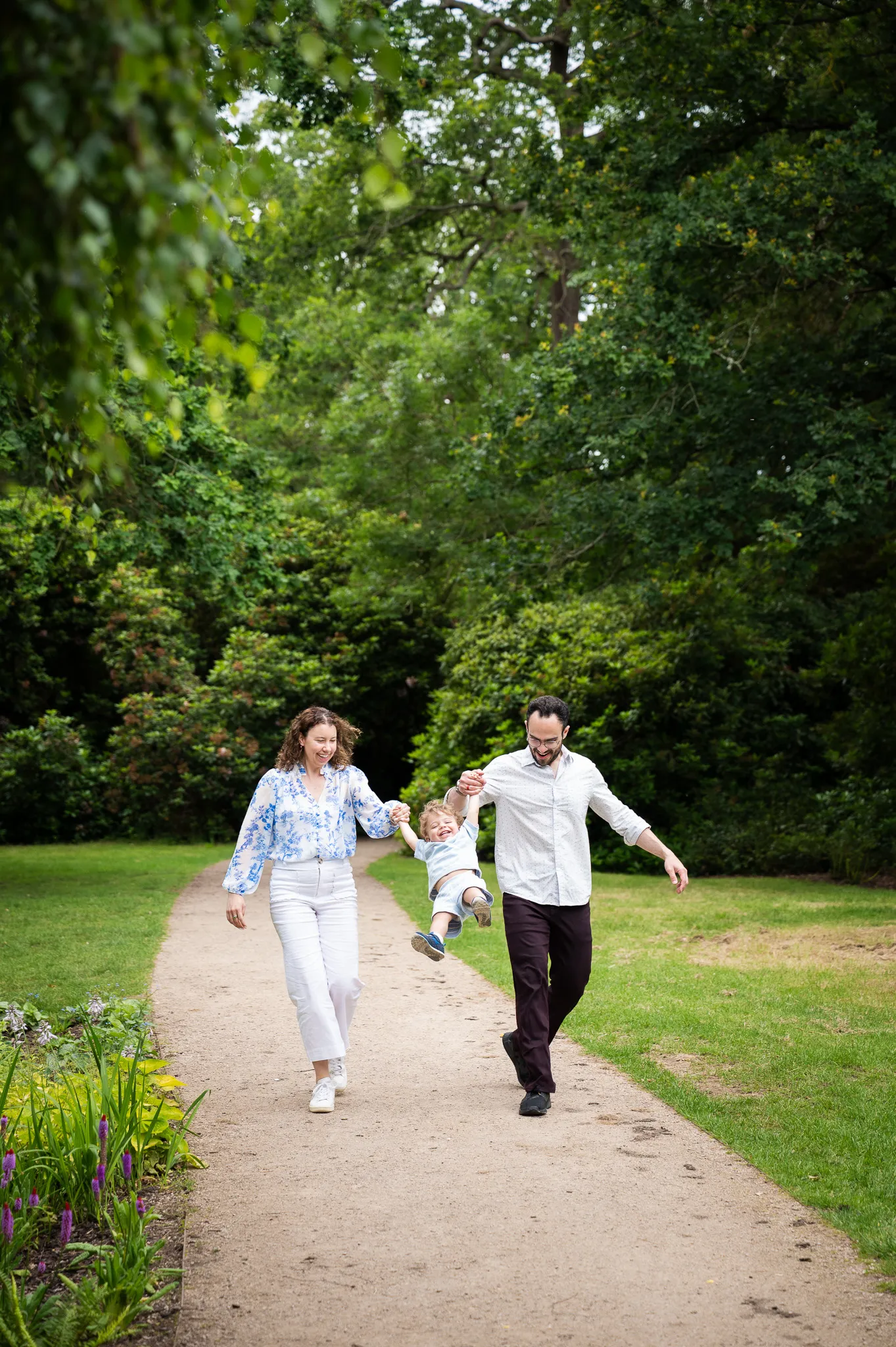 Parents swinging their toddler between them along a leafy garden path
