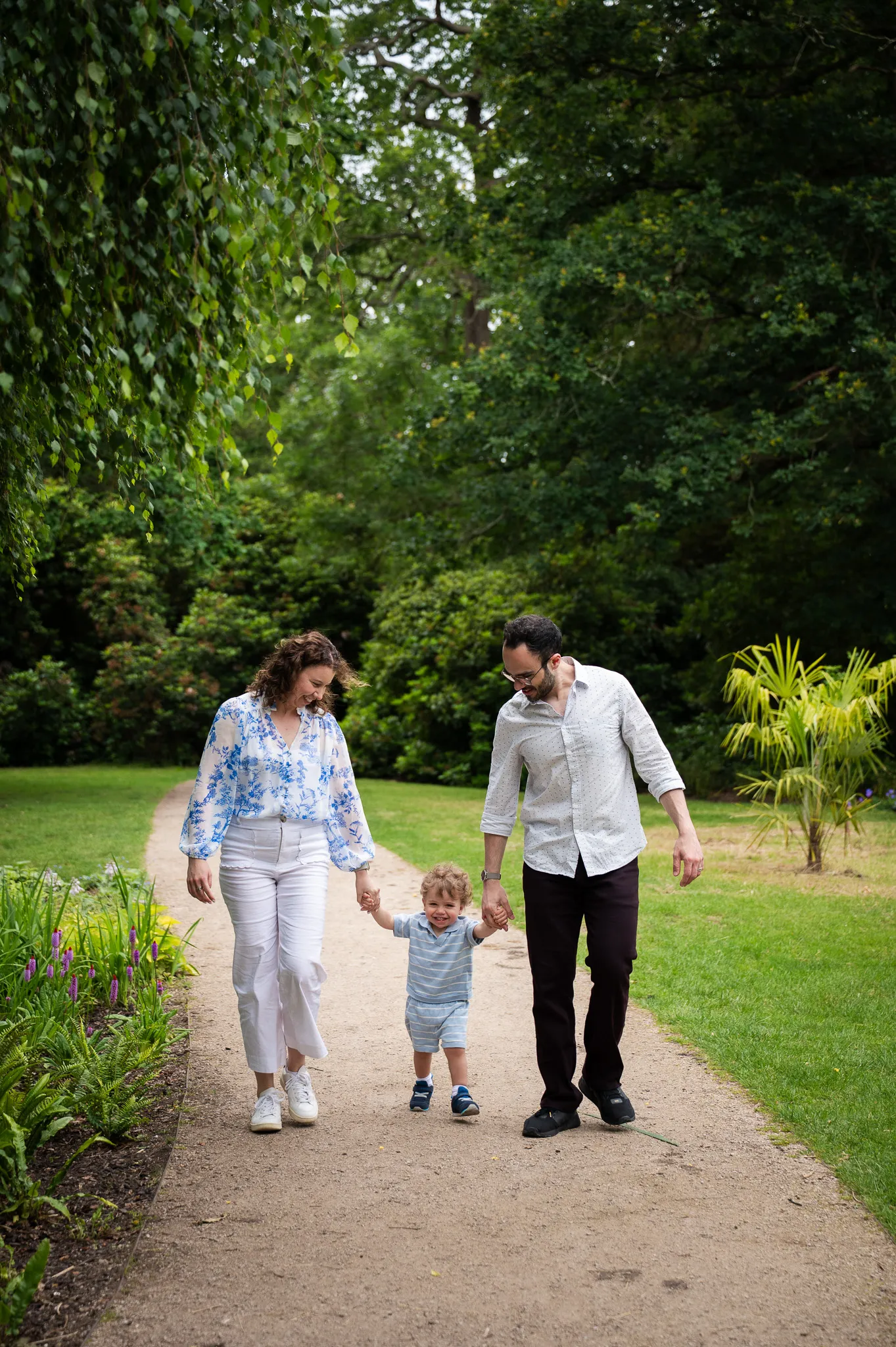 Parents walking hand in hand with their toddler along a garden path