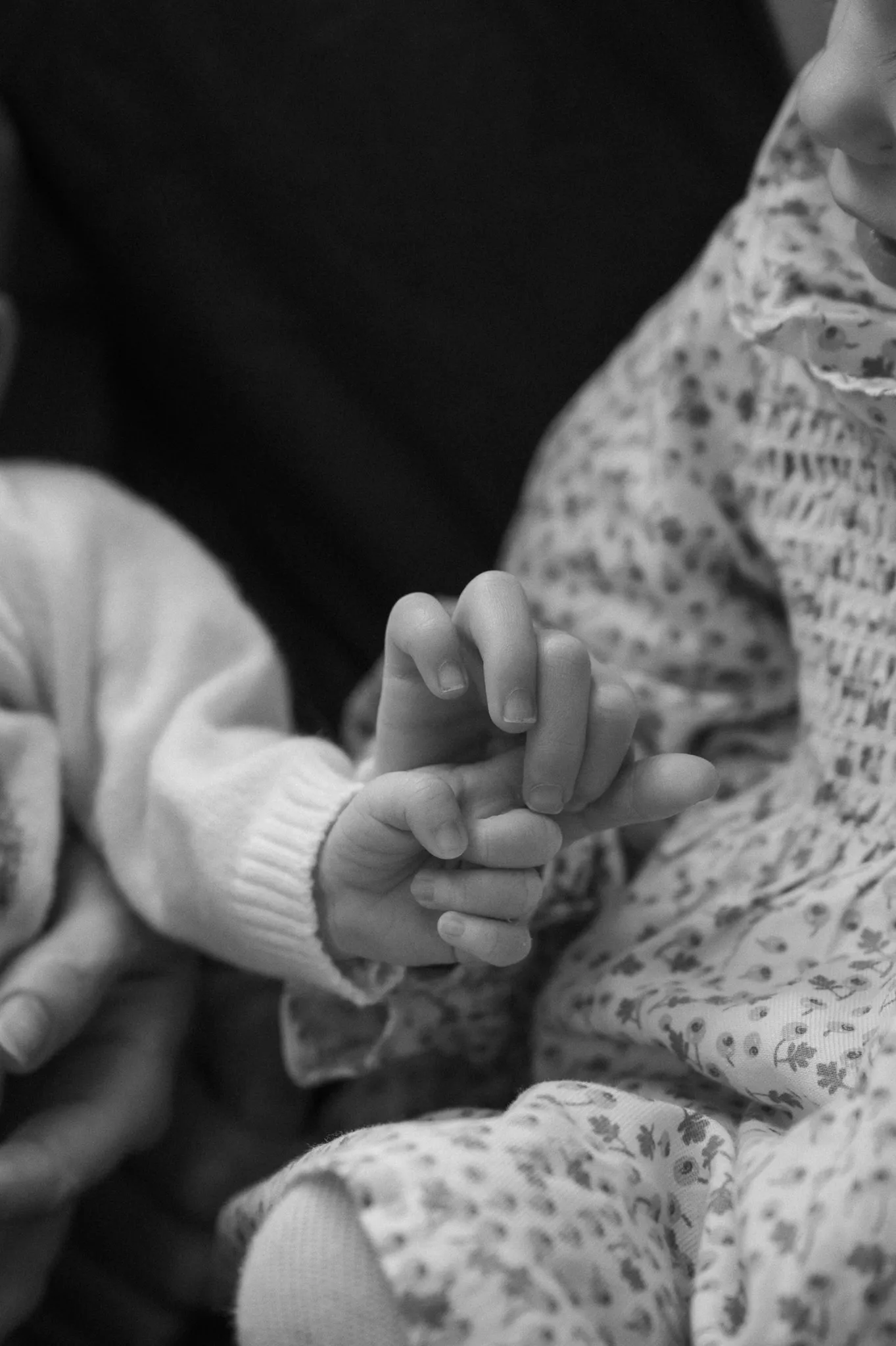 Black and white close-up of big sister holding her newborn sibling's hand