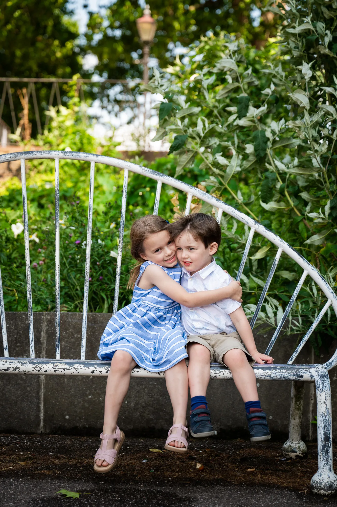 Big sister cuddling her little brother on a garden bench