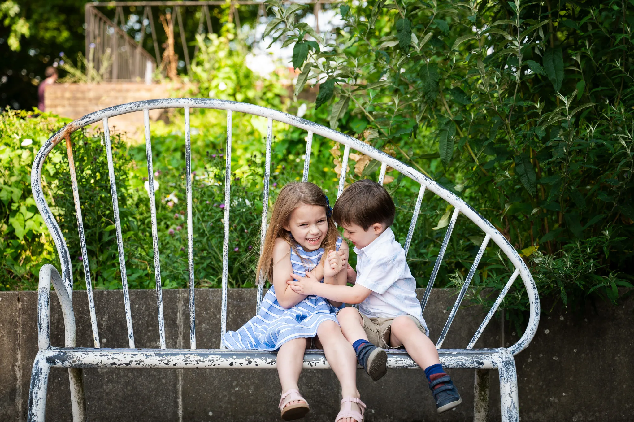 Brother and sister hugging and laughing on a garden bench