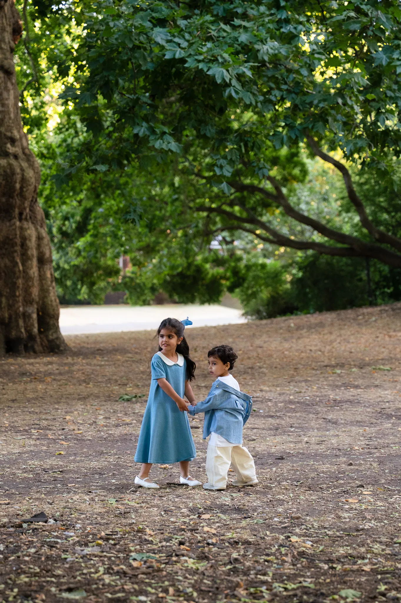Little sister and brother playing together on a sunny park path