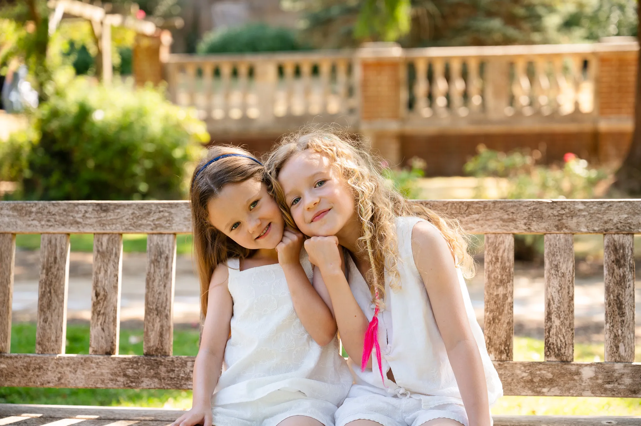 Two sisters resting their heads together and smiling on a wooden garden bench