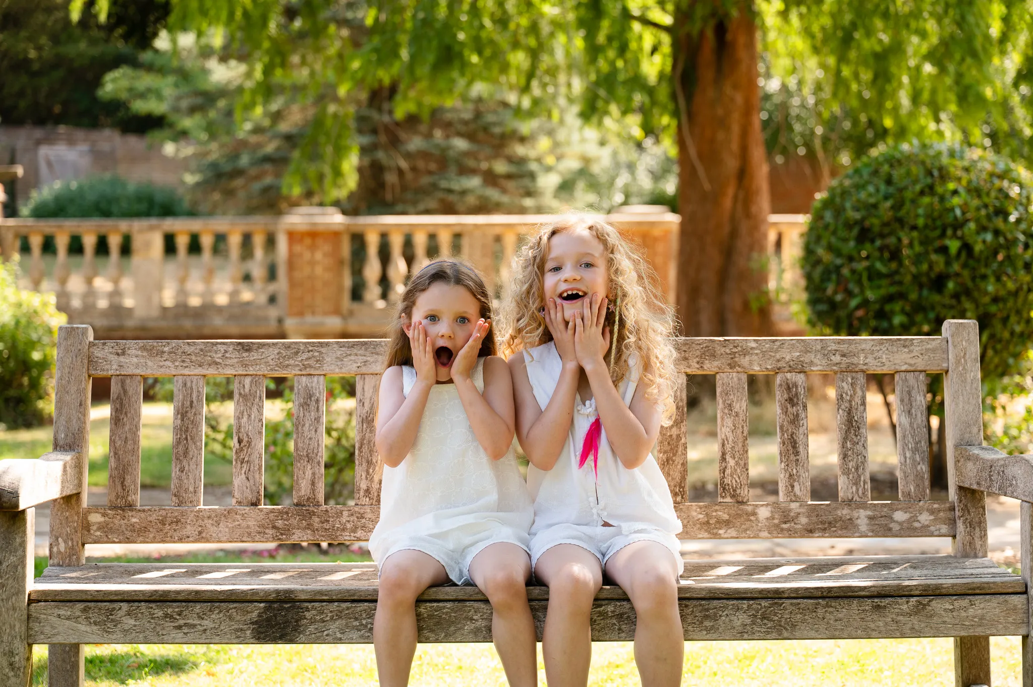 Two sisters pulling surprised faces on a wooden garden bench