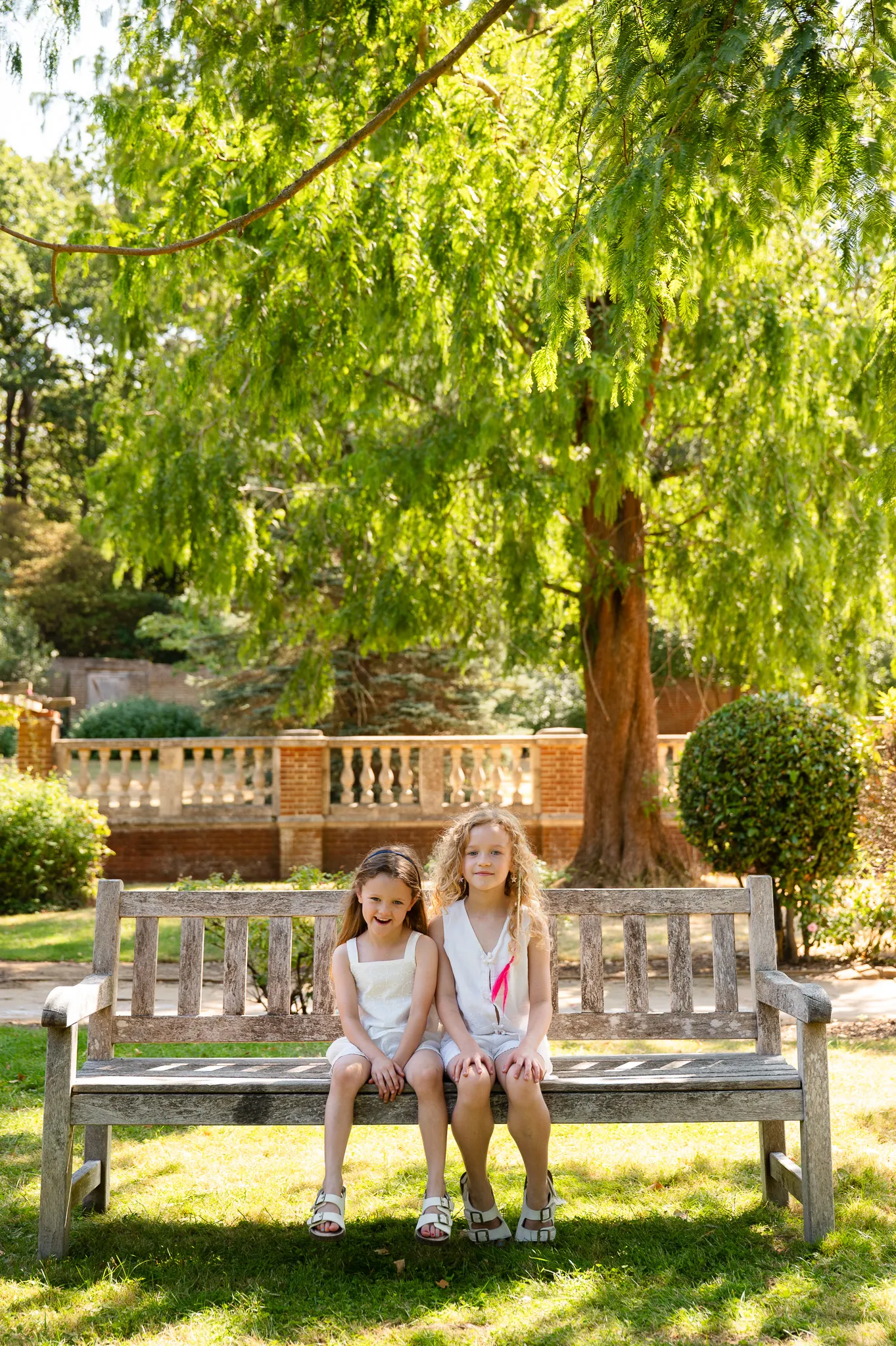 Two sisters sitting together on a wooden bench in a walled garden