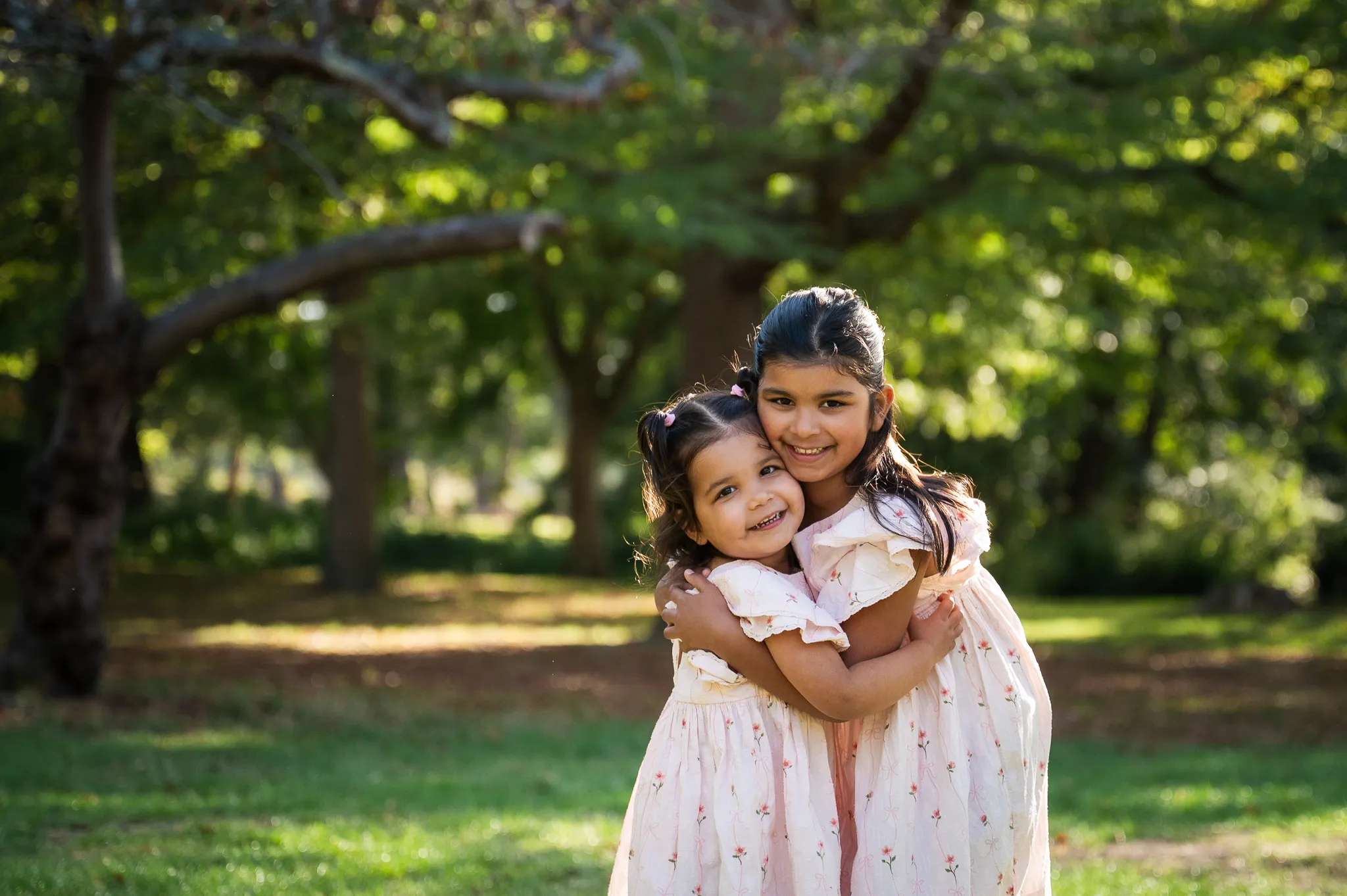 Two sisters hugging and smiling under the trees