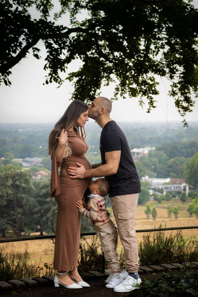 Husband and wife kissing, expecting another child, little boy kissing mum's tummy